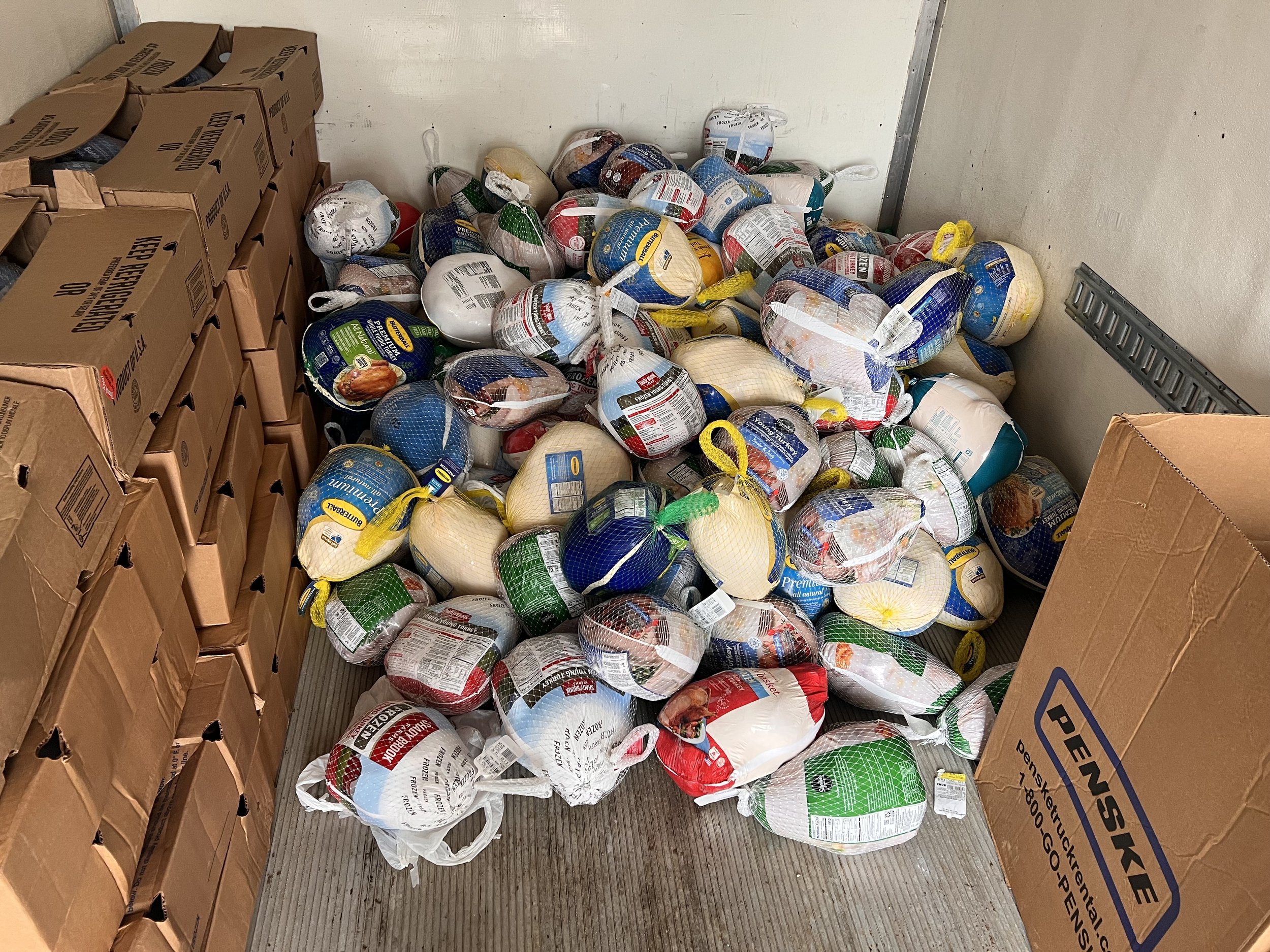 Piles of packaged frozen chickens in a storage room corner with cardboard boxes on one side.