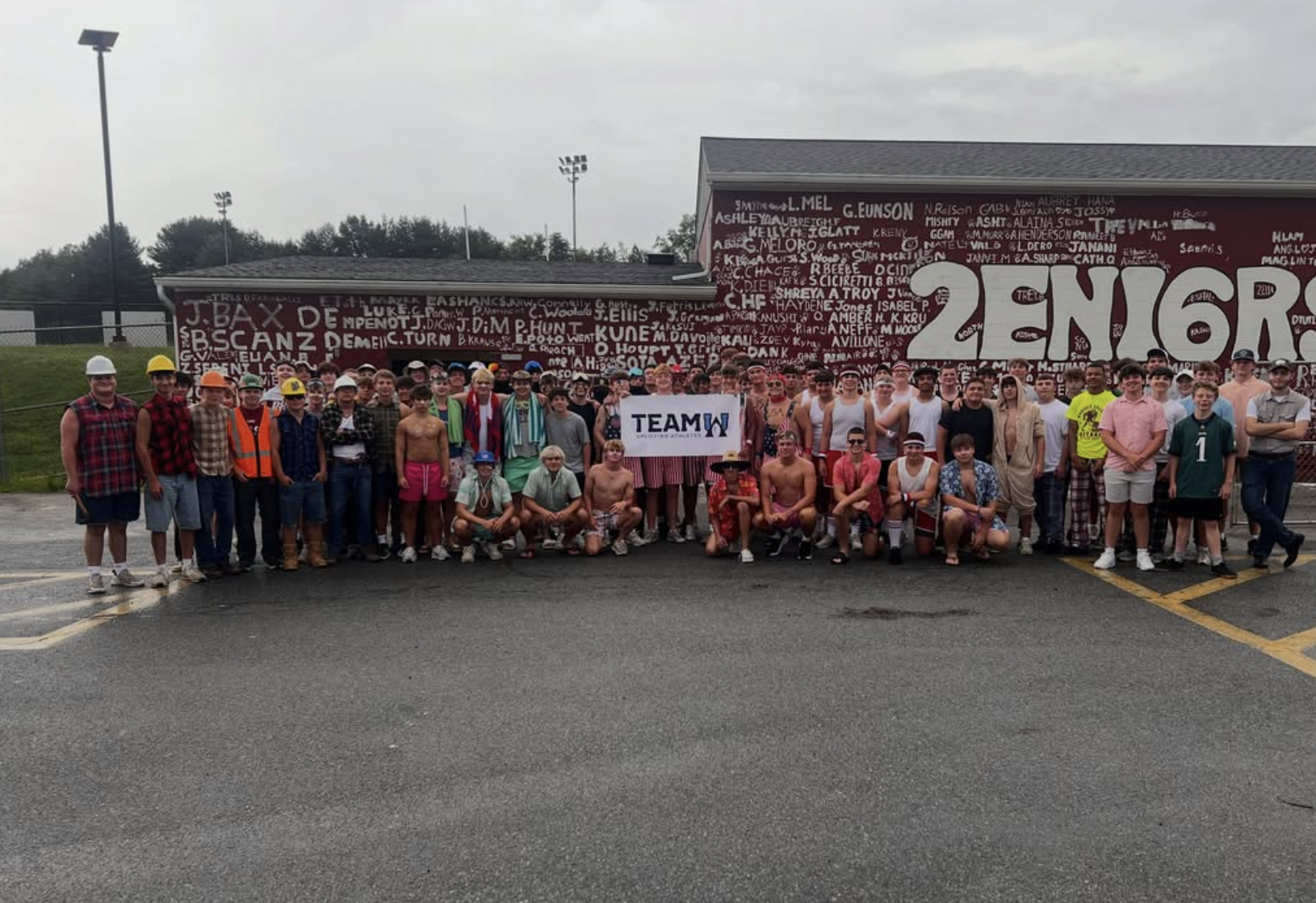 Group of people in casual and construction attire standing in front of a maroon wall with white graffiti text and a large white sign that says "TEAM".