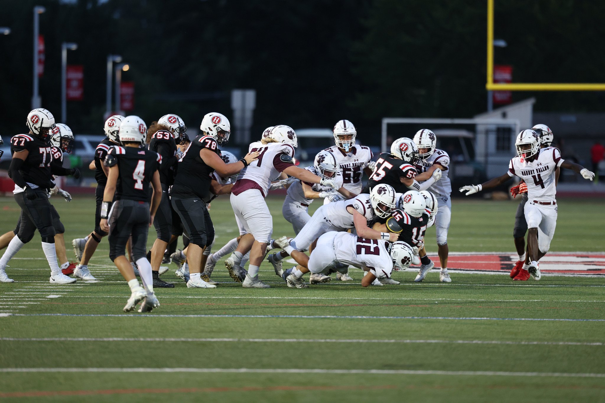 American football game with players on the field, some players are blocking while others are tackling, during a play on a football field with goalpost in the background.