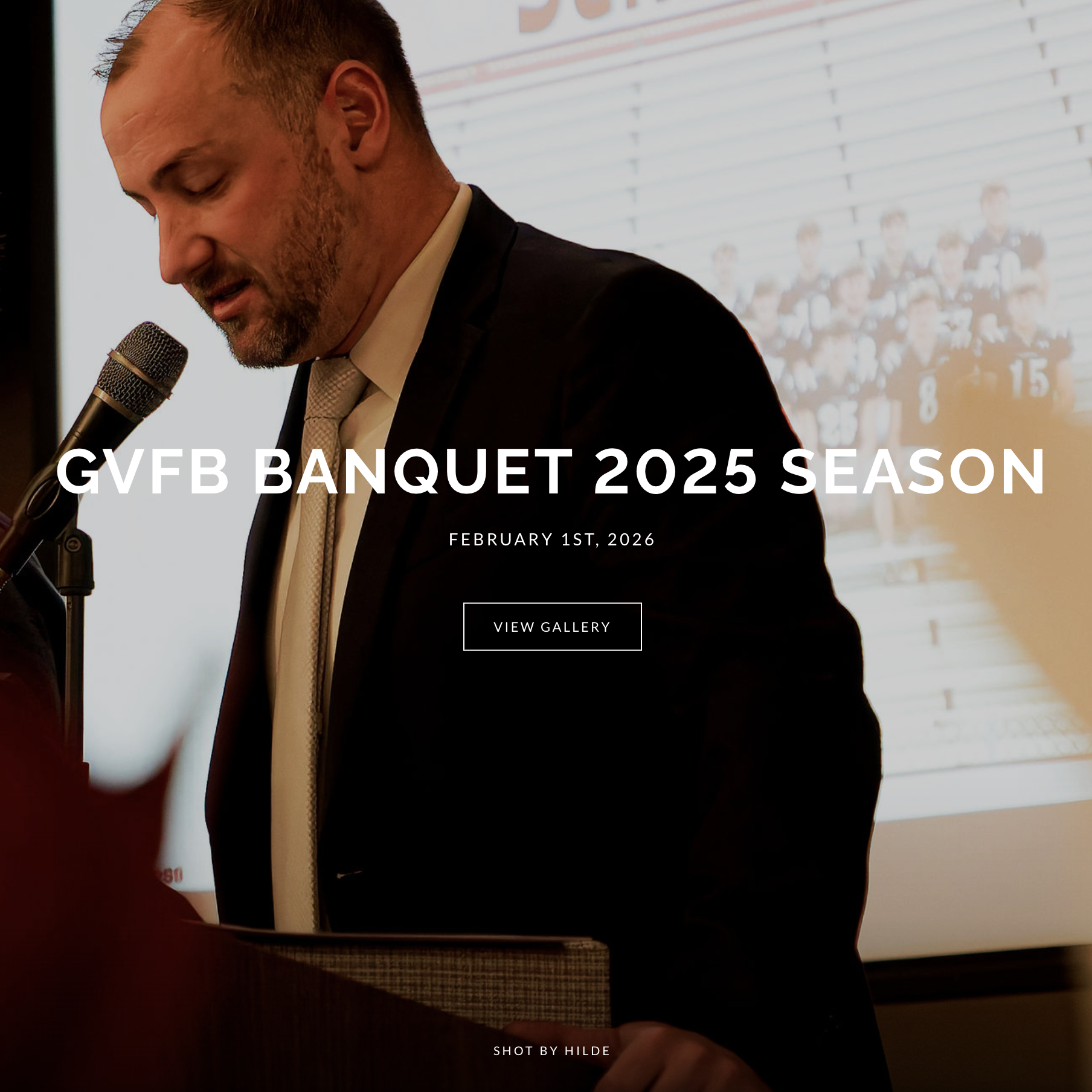 A man in a suit and tie speaking into a microphone at a formal event, with a projection of a sports team in the background, overlaid with the text "GVFB Banquet 2025 Season," scheduled for February 1st, 2026.