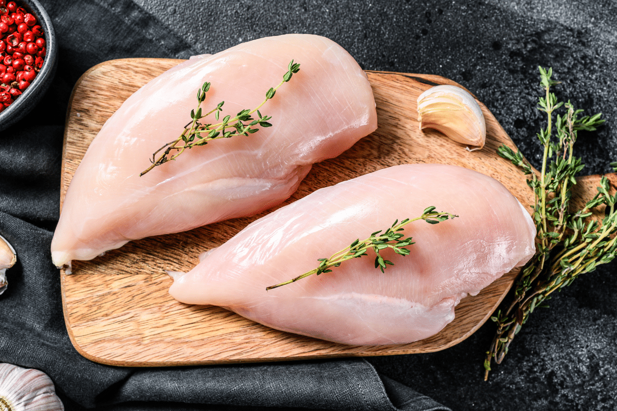 20250407-how-to-cook-boneless-skinless-chicken-breast-on-a-cutting-board-with-thyme-garlic-and-red-peppercorns.png