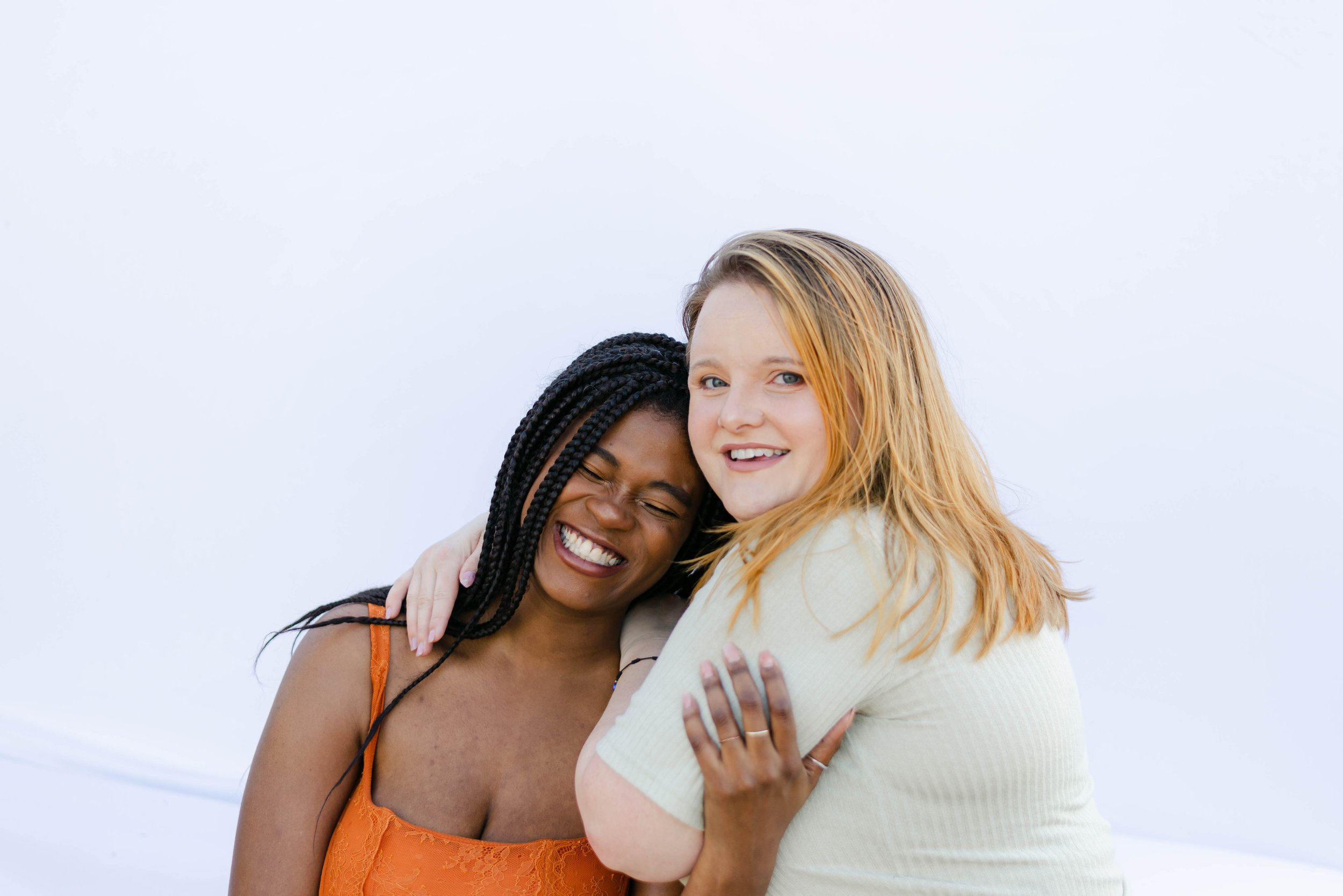 The founders of Post Glow Studio share a joyful moment, hugging and laughing in front of a clean white backdrop. Their warmth and genuine connection reflect the heart behind their creative collaboration.