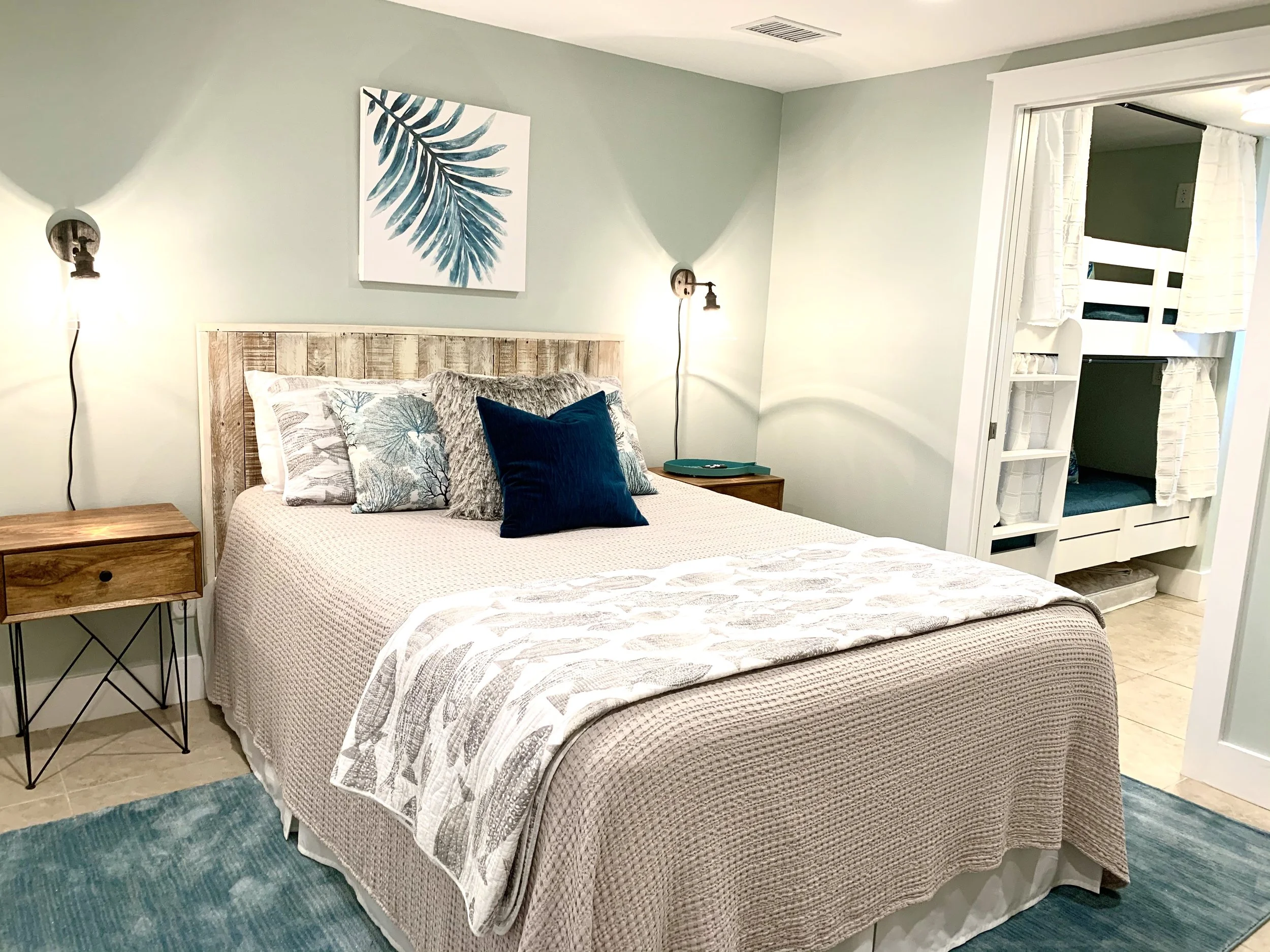 A bedroom with a bed, pillows, bedside tables, wall-mounted lamps, a wall art print, and an open closet with ladder-like shelves