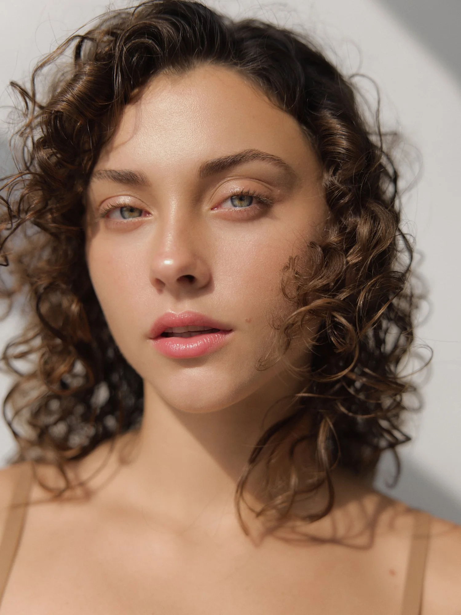 Close-up of a woman with curly brown hair, light skin, blue eyes, and pink lips, looking slightly to the side.