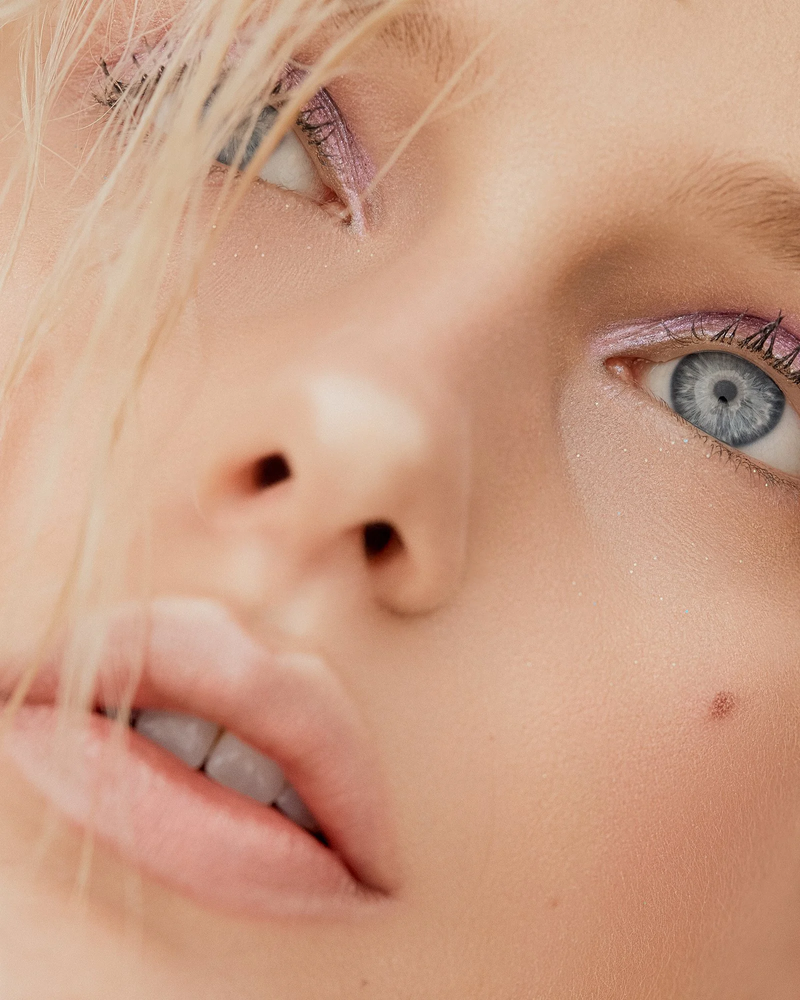 A close-up of a person's face, focusing on one eye with eye makeup, freckles, and blonde hair falling across the face.
