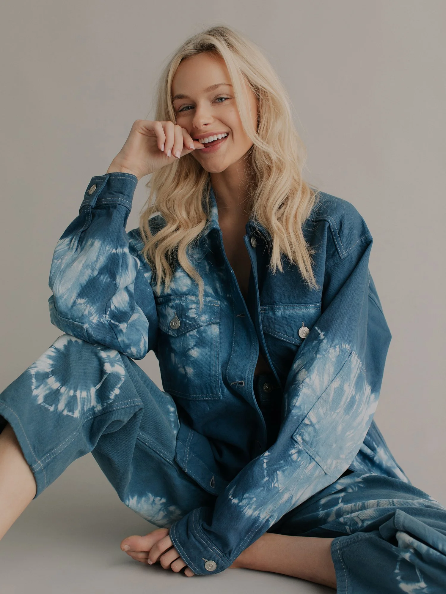 A young woman with blonde wavy hair wearing a blue tie-dye denim jacket smiling and looking at the camera.