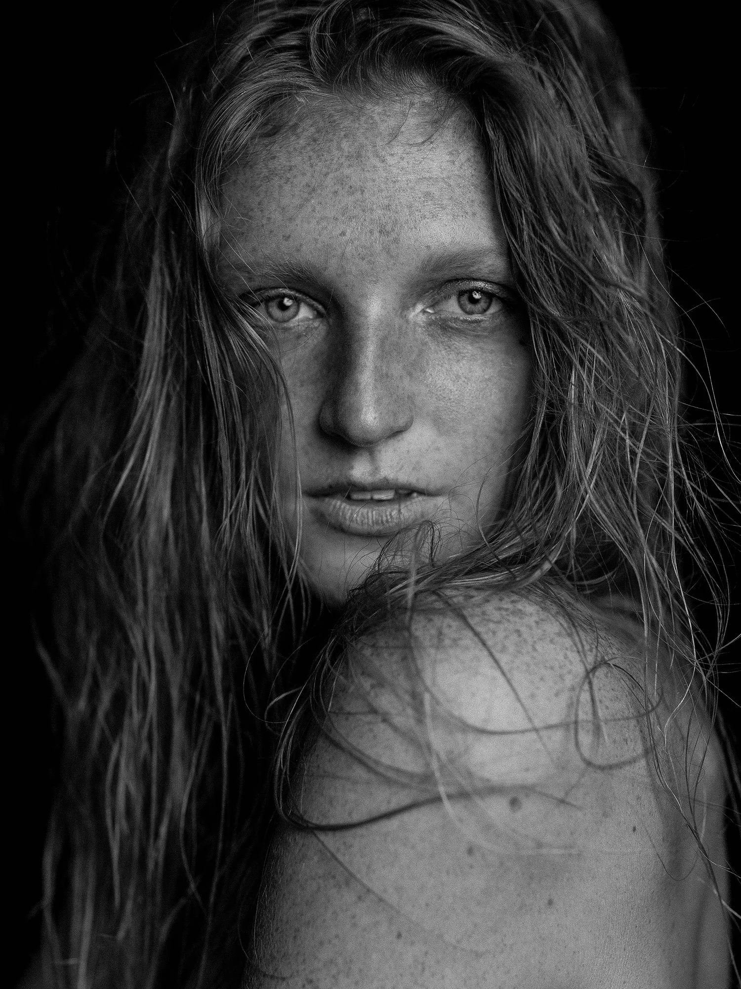 Close-up of a woman's face with light-colored eyes and long, wavy hair, partially covering her face, black and white photograph.