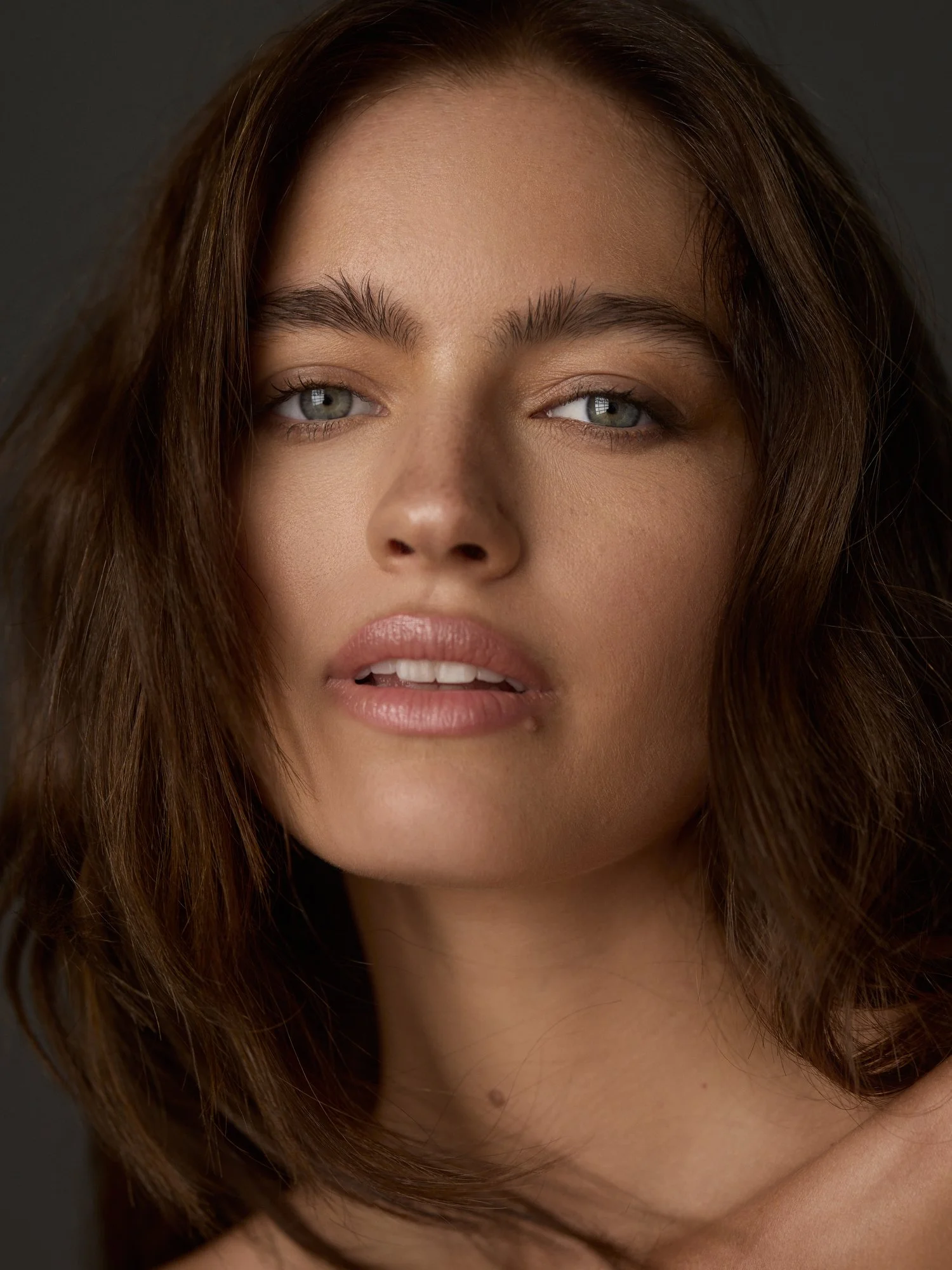 Close-up of a woman's face with wavy brown hair, blue eyes, and natural makeup.