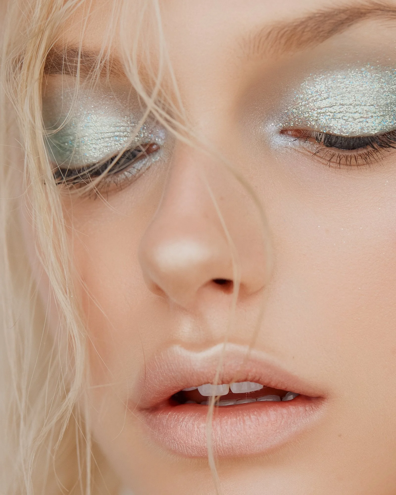 Close-up of a woman's face, focusing on her eye makeup with glittery eyeshadow, partially closed eye, and hair.