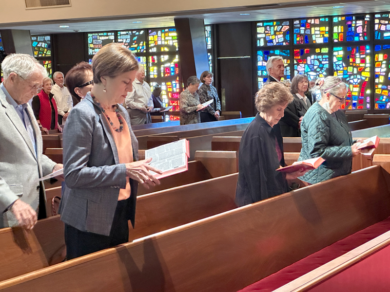 People praying or reading during a church service inside a church with stained glass windows.