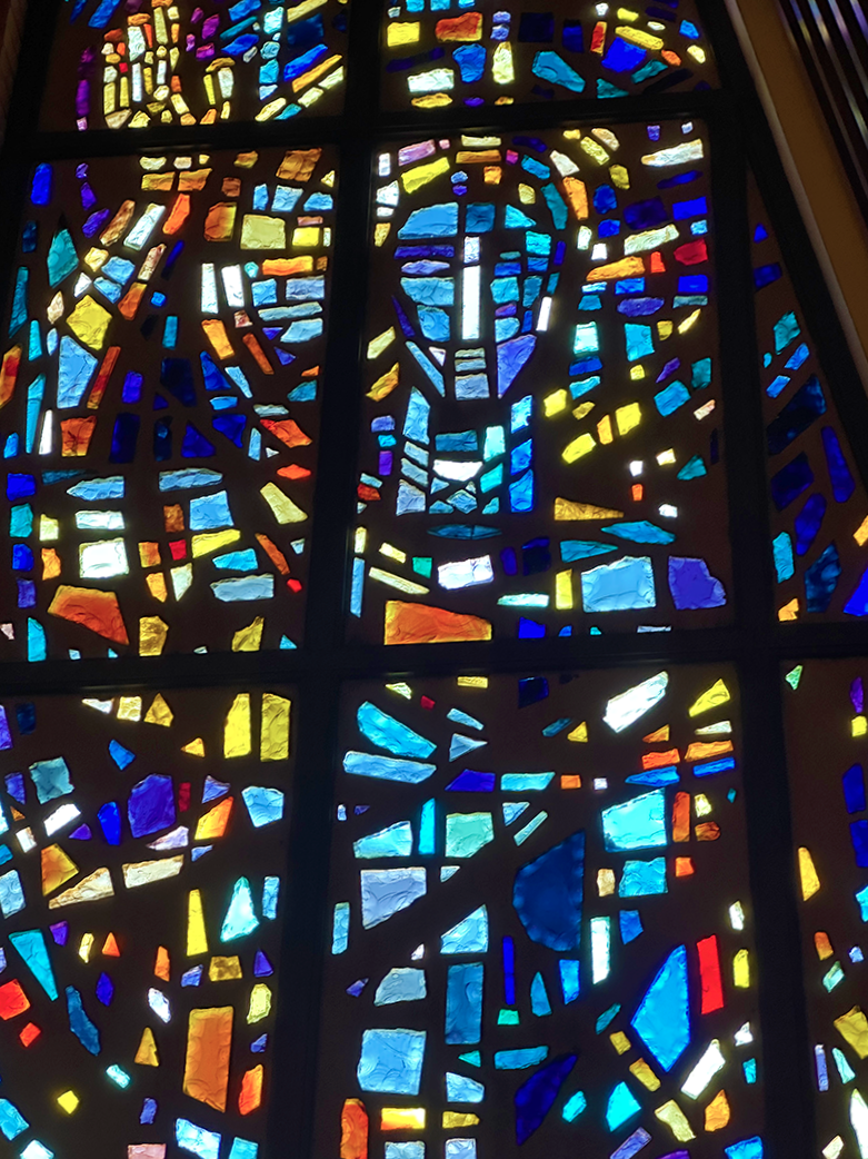Colorful stained glass window depicting Jesus Christ, with a halo, in a mosaic style.
