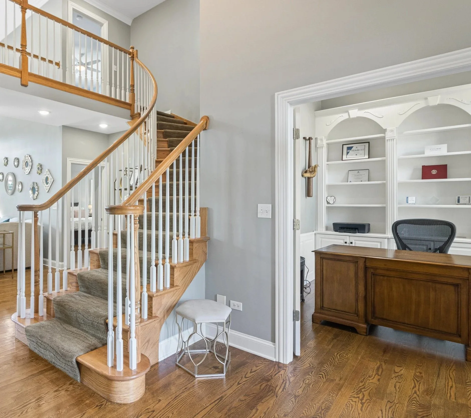 Interior view of a house with a wooden staircase and a home office or study area with built-in white shelving.