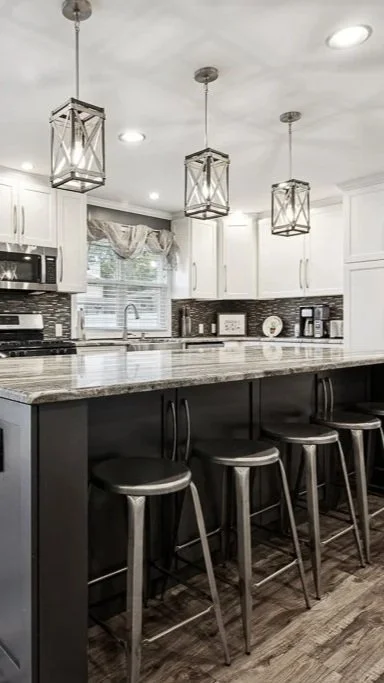 Modern kitchen with white upper cabinets, dark lower cabinets, a marble countertop island, three pendant lights, and four bar stools.