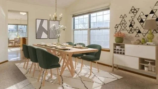 Dining room with a wooden table, six dark green chairs, a geometric black and white wall art, a white sideboard with vases, a large window, a chandelier, and a patterned rug.