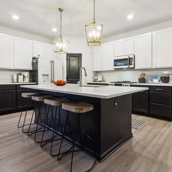Modern kitchen with black and white cabinetry, island with white countertop, four wooden stools, and two pendant lights.