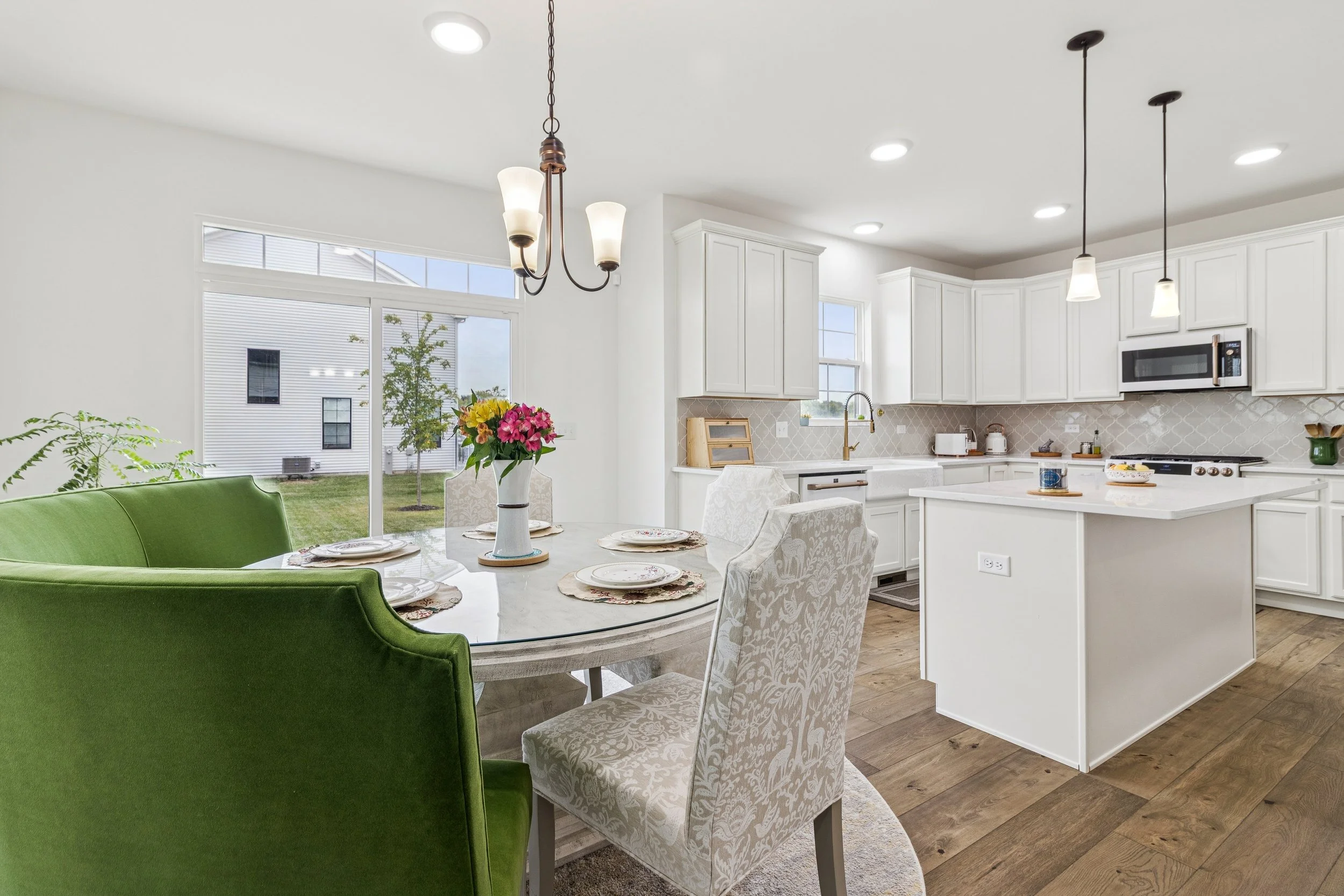 Open-concept kitchen and dining area with white cabinetry, marble countertops, hardwood floors, and a round table set with fine china and a floral centerpiece.