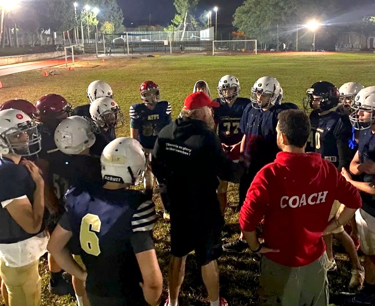 Kadoorie football players and coaches gathered on a field at night during a practice.