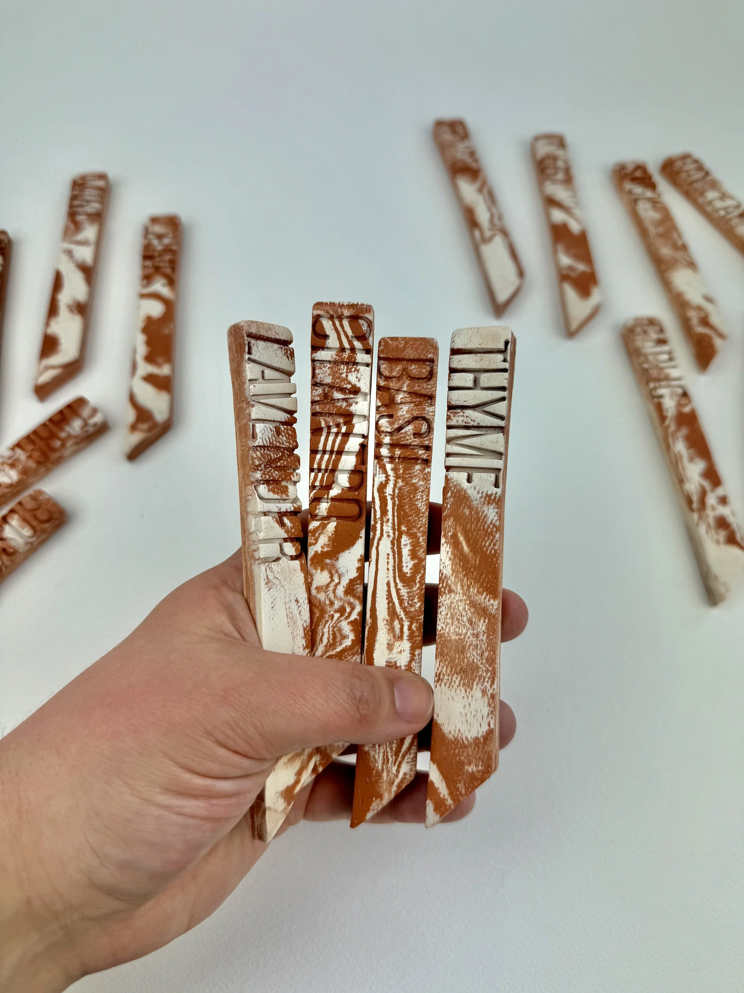 Multiple caramel and white marbled stamps on wooden blocks, held in hand, with more scattered on white surface.