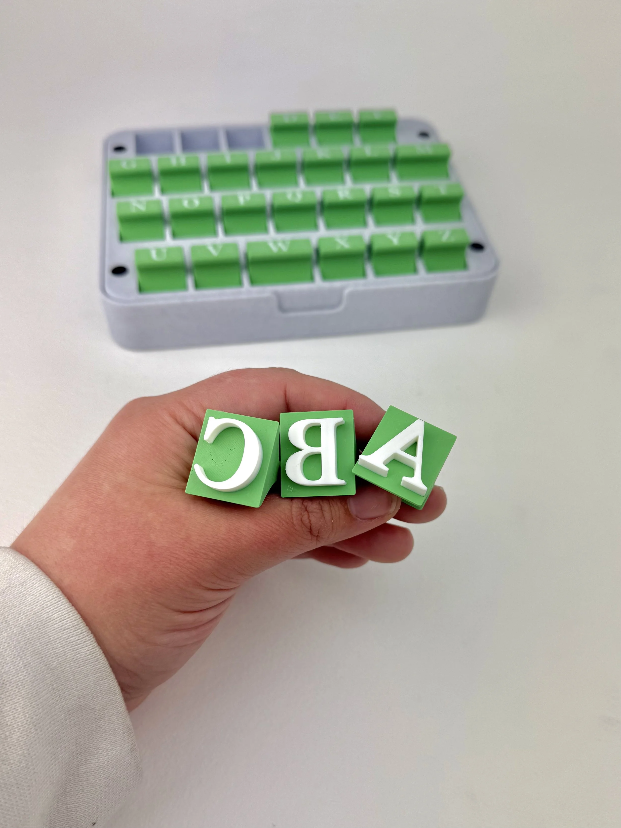 Person holding green alphabet blocks spelling "ABC" with a gray box of similar blocks in the background.