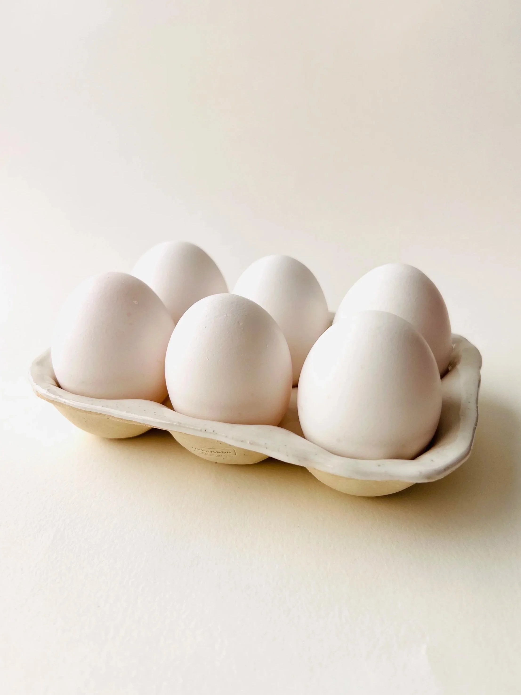 Six white eggs in a white egg carton on a light background.