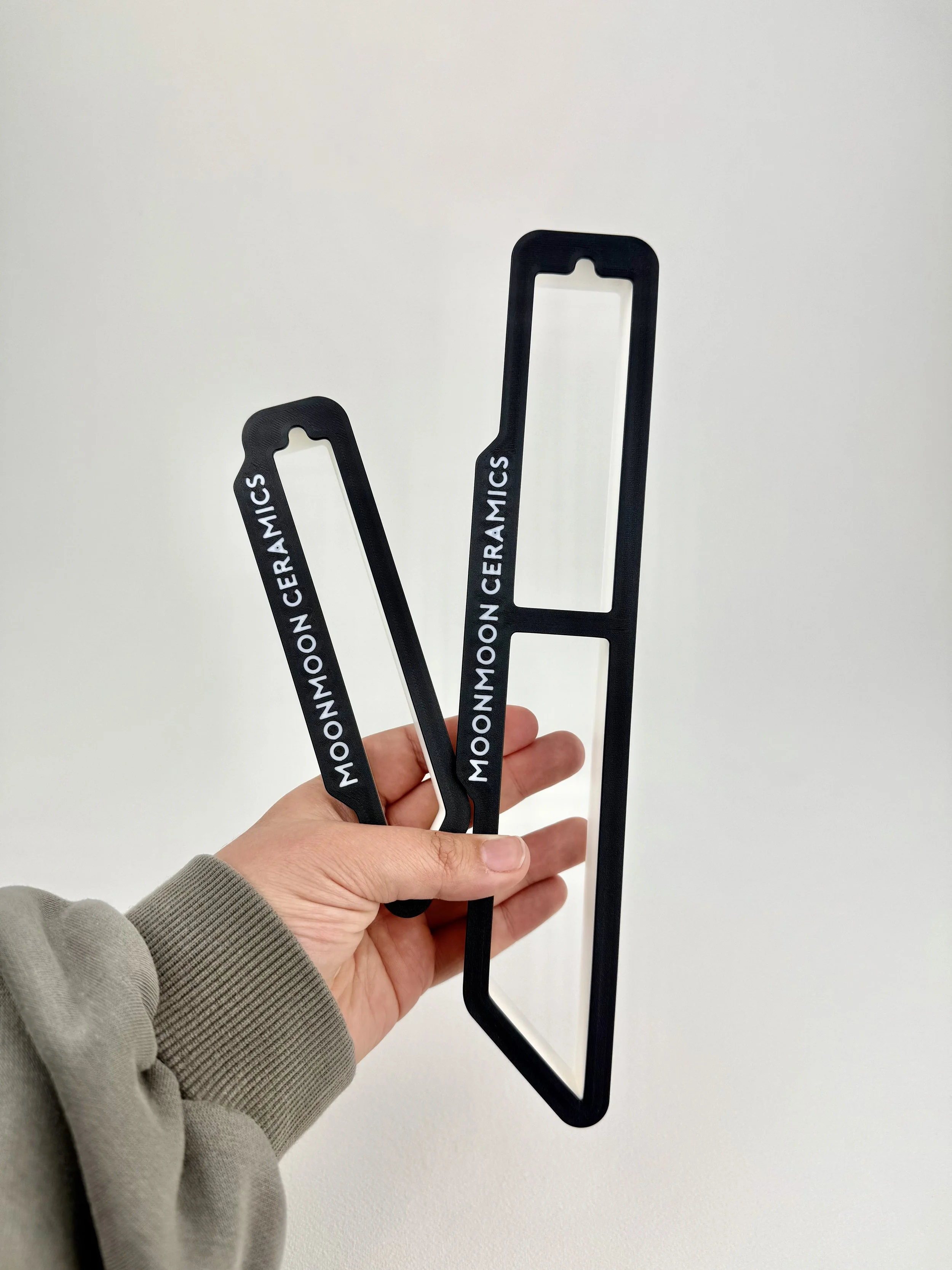 Two black ceramic slimming tools with the words 'MOON MOON CERAMICS' written on them, held by a person's hand against a white background.