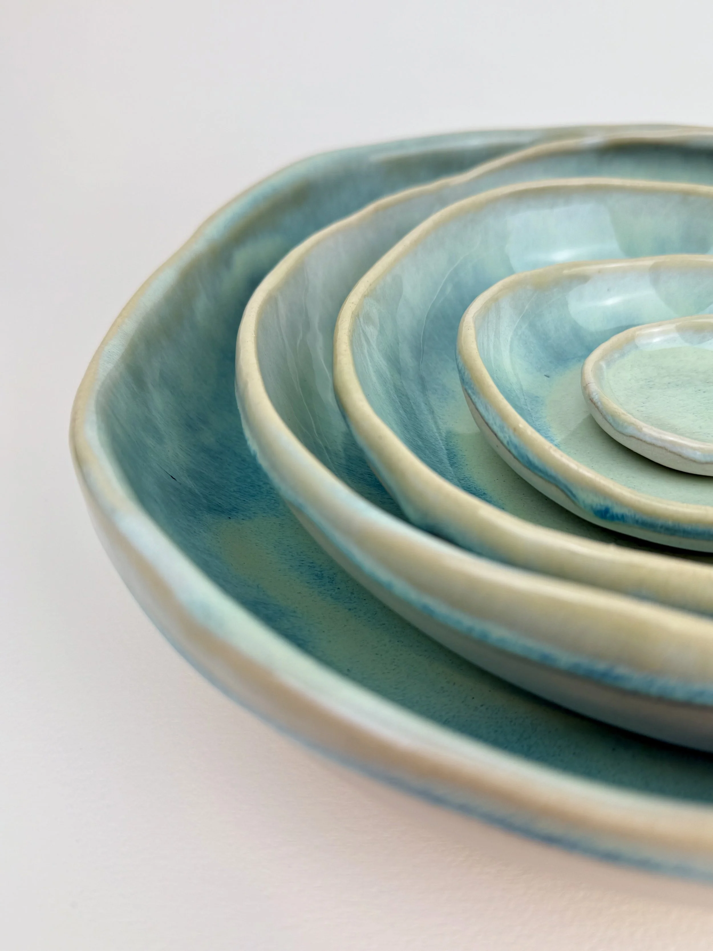 A set of nested ceramic bowls in shades of blue and green, placed inside each other on a white background.