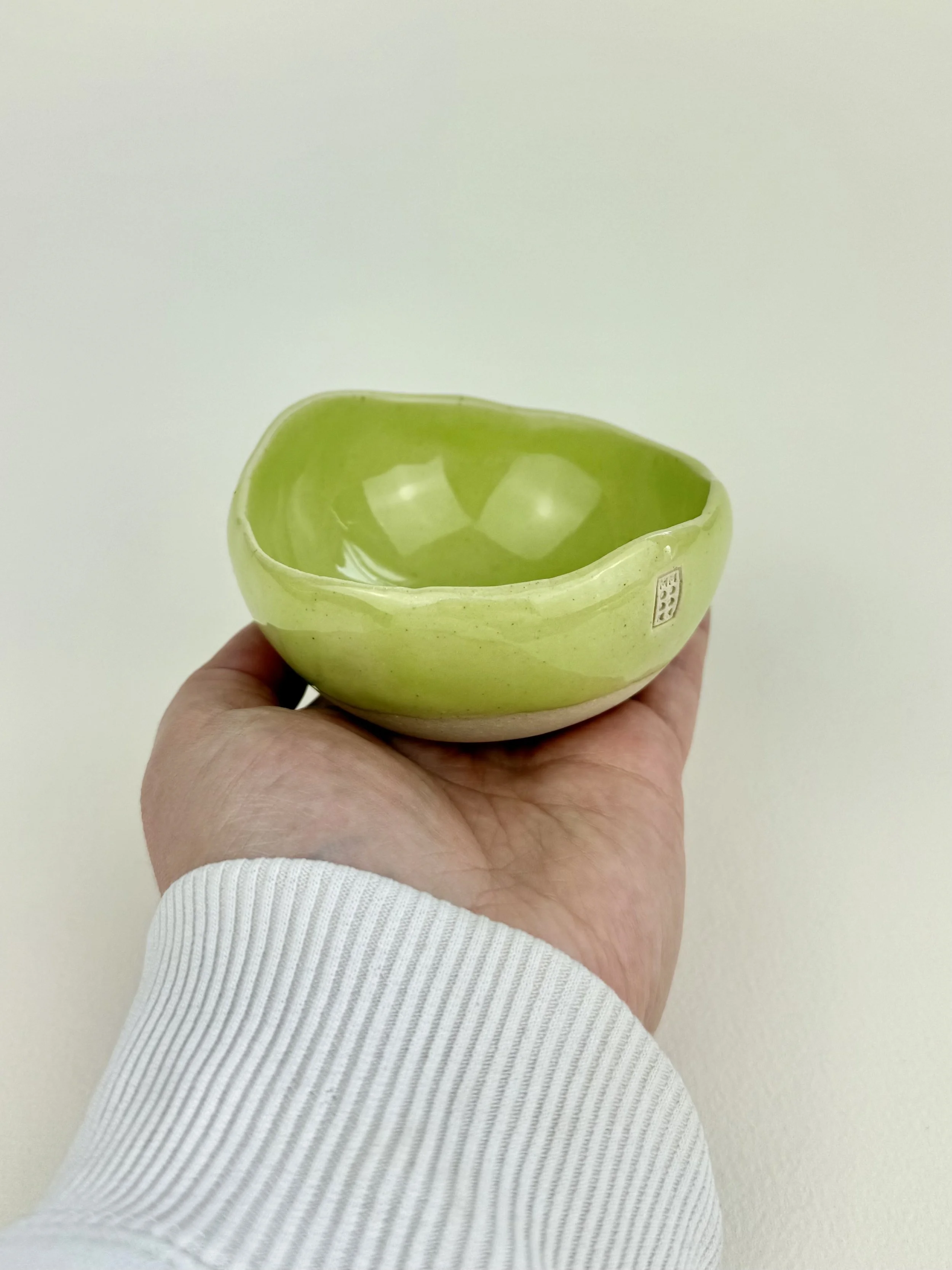 Green ceramic bowl held by a hand against a plain, light background.