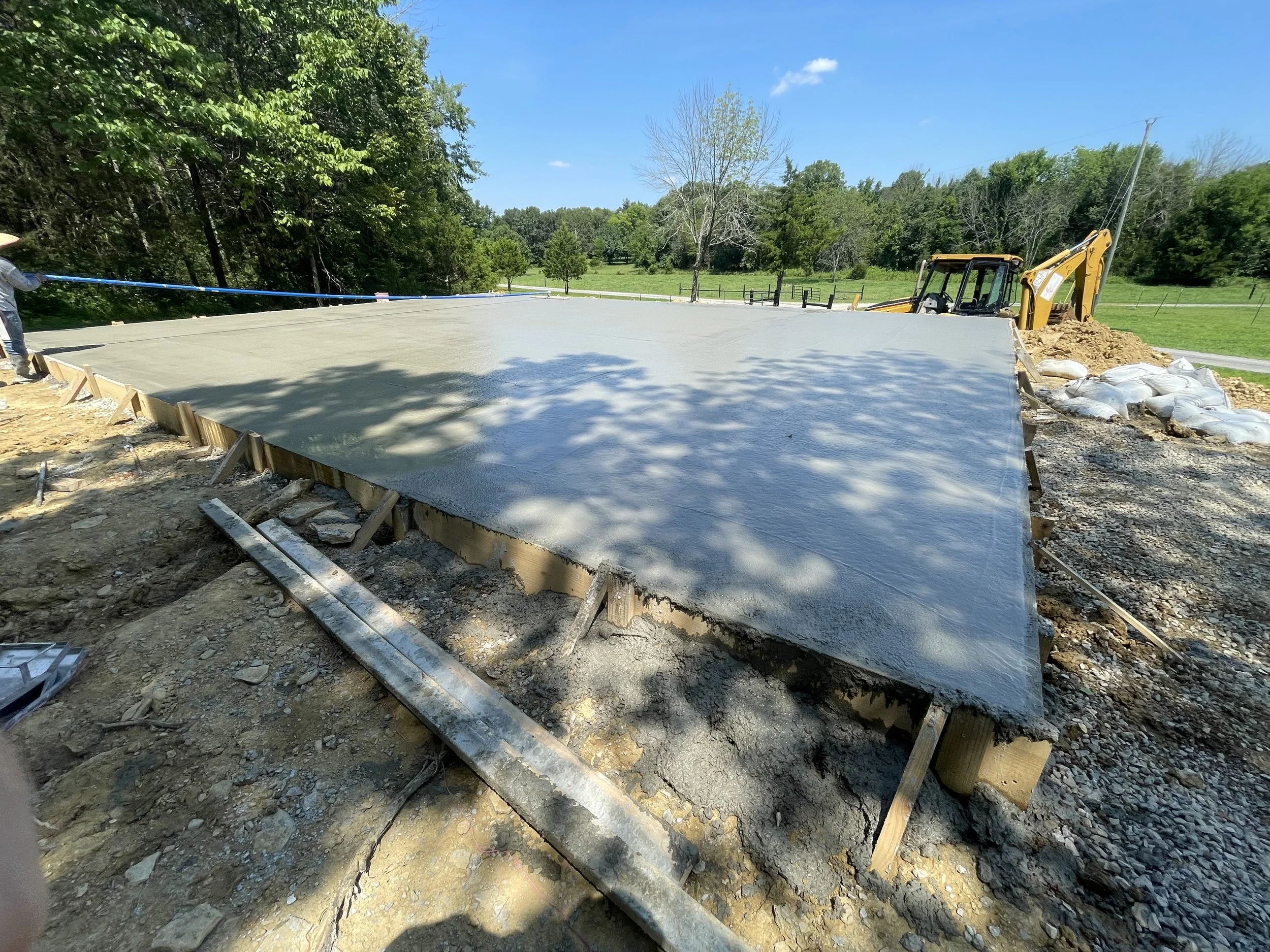 Concrete slab being poured on a construction site with trees and blue sky in the background.