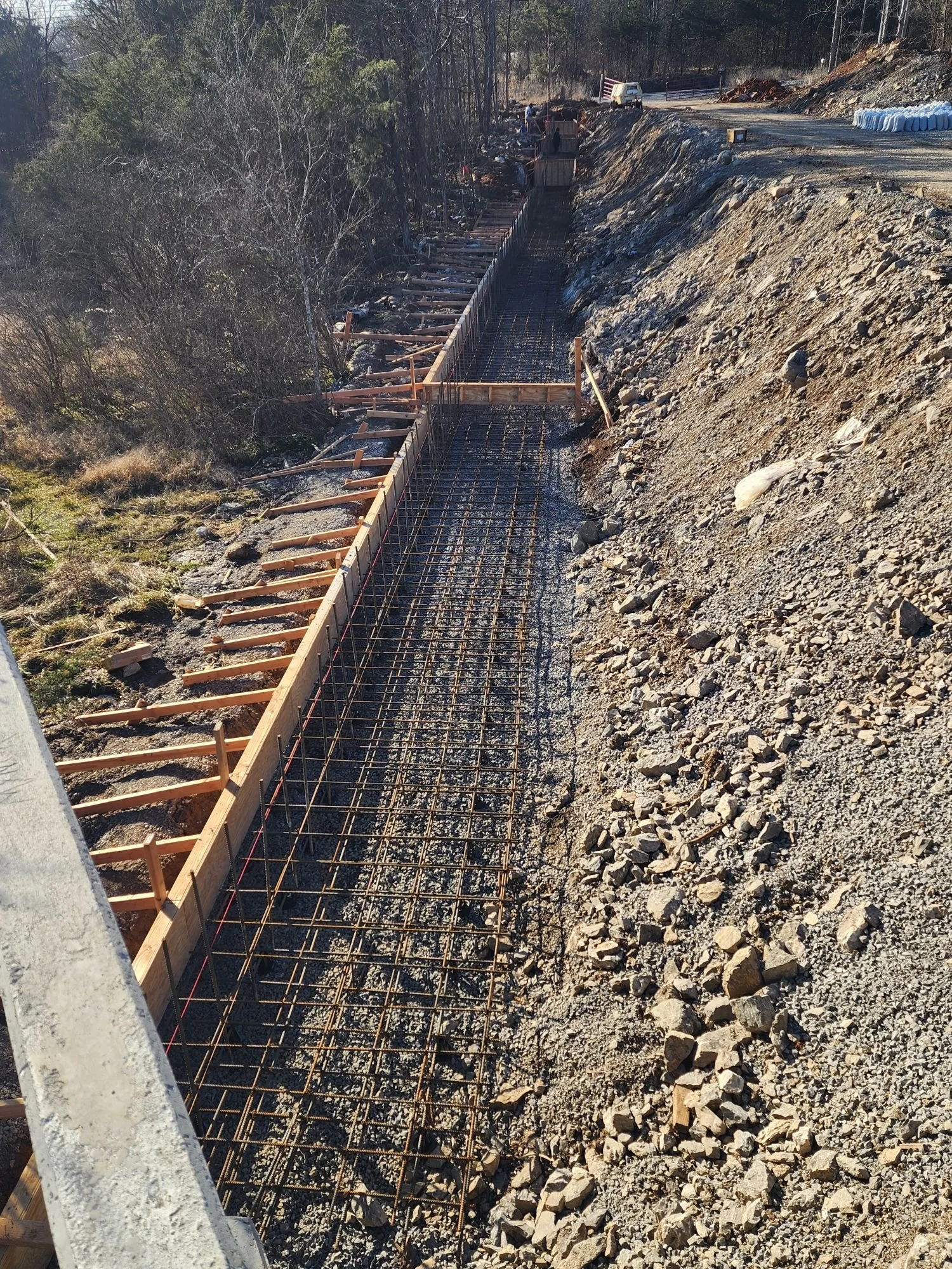 Construction site with rebar and wooden formwork for a concrete wall or foundation on a sloped hillside.