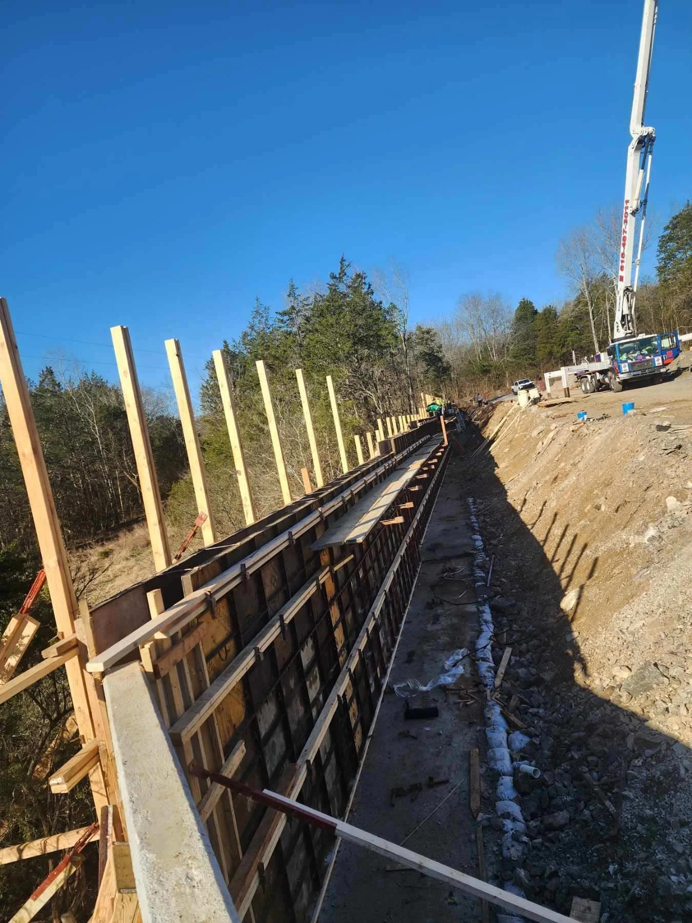 Construction site with a partially built retaining wall, wooden forms, and a crane on a clear day.