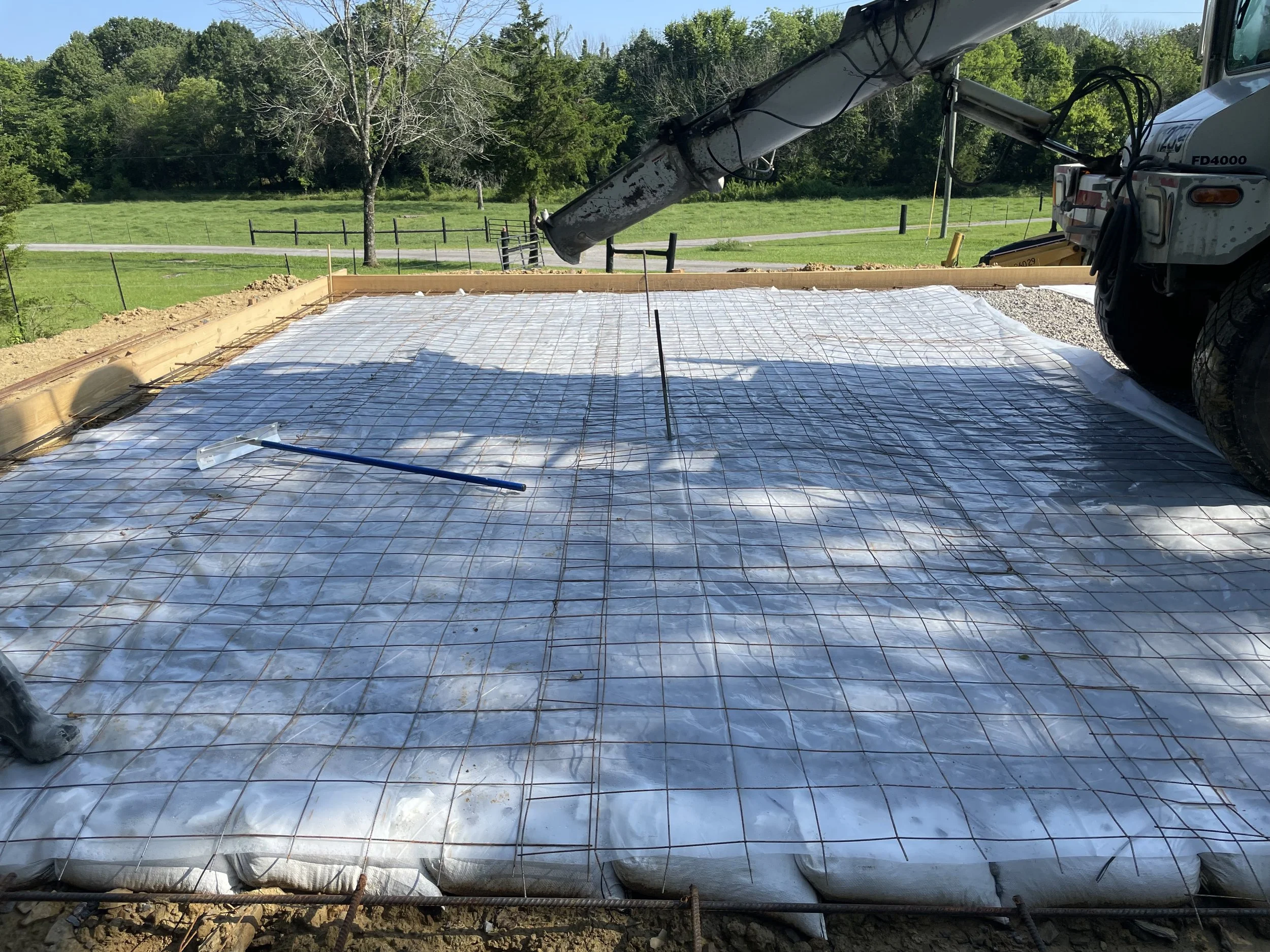 Construction site with a concrete foundation prepared with plastic sheeting, rebar grid, and a concrete pump truck ready for pouring.