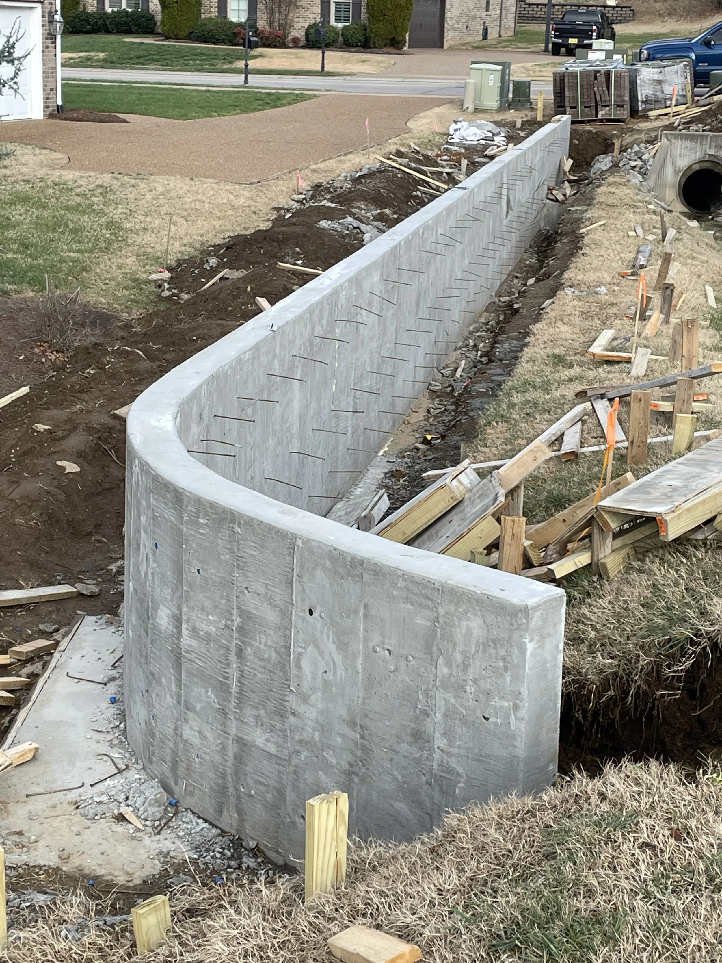 Construction site with a newly built curved concrete wall, wooden forms and construction materials around it.