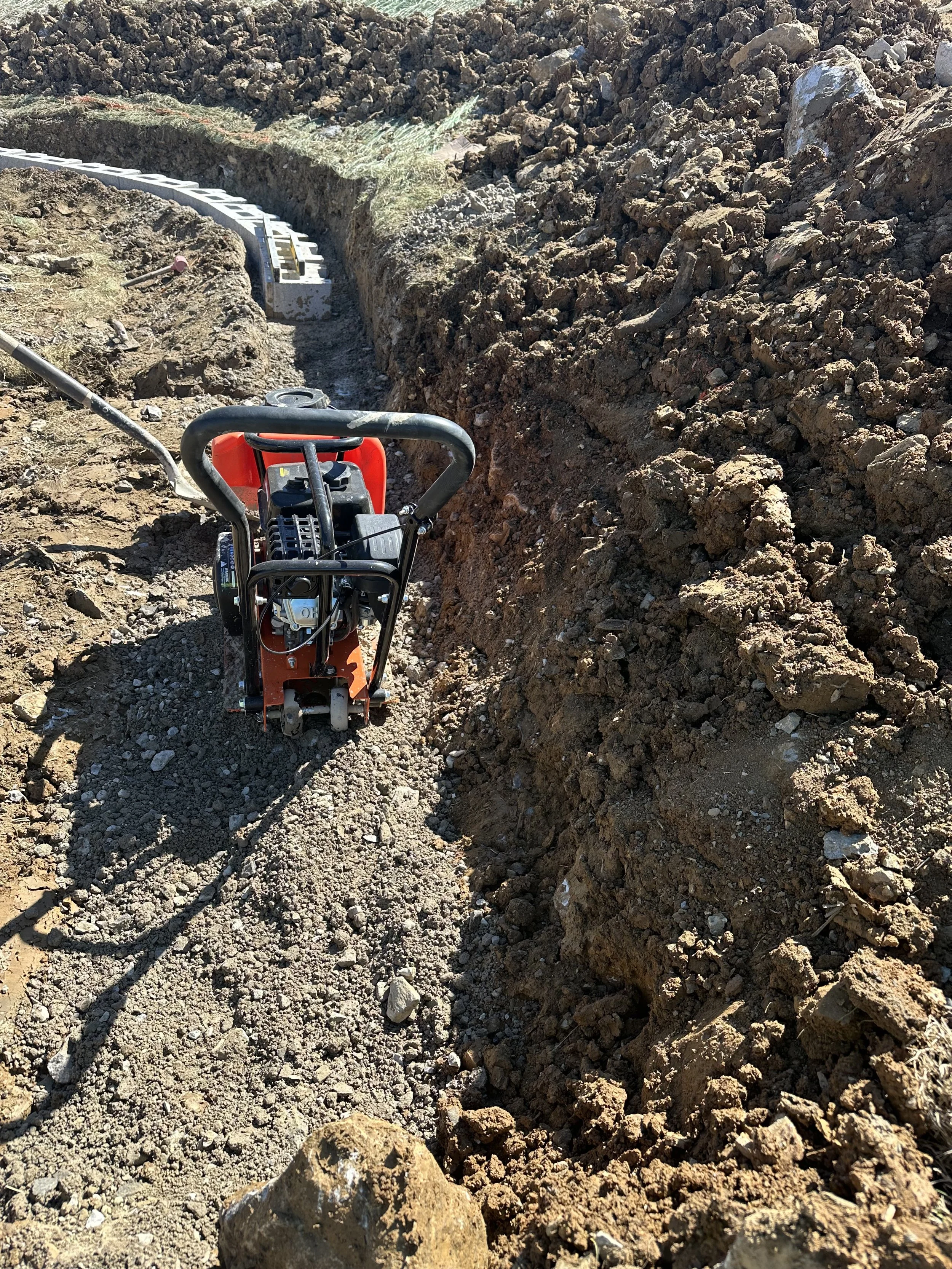 A small construction compactor machine working in a dirt trench at a construction site.