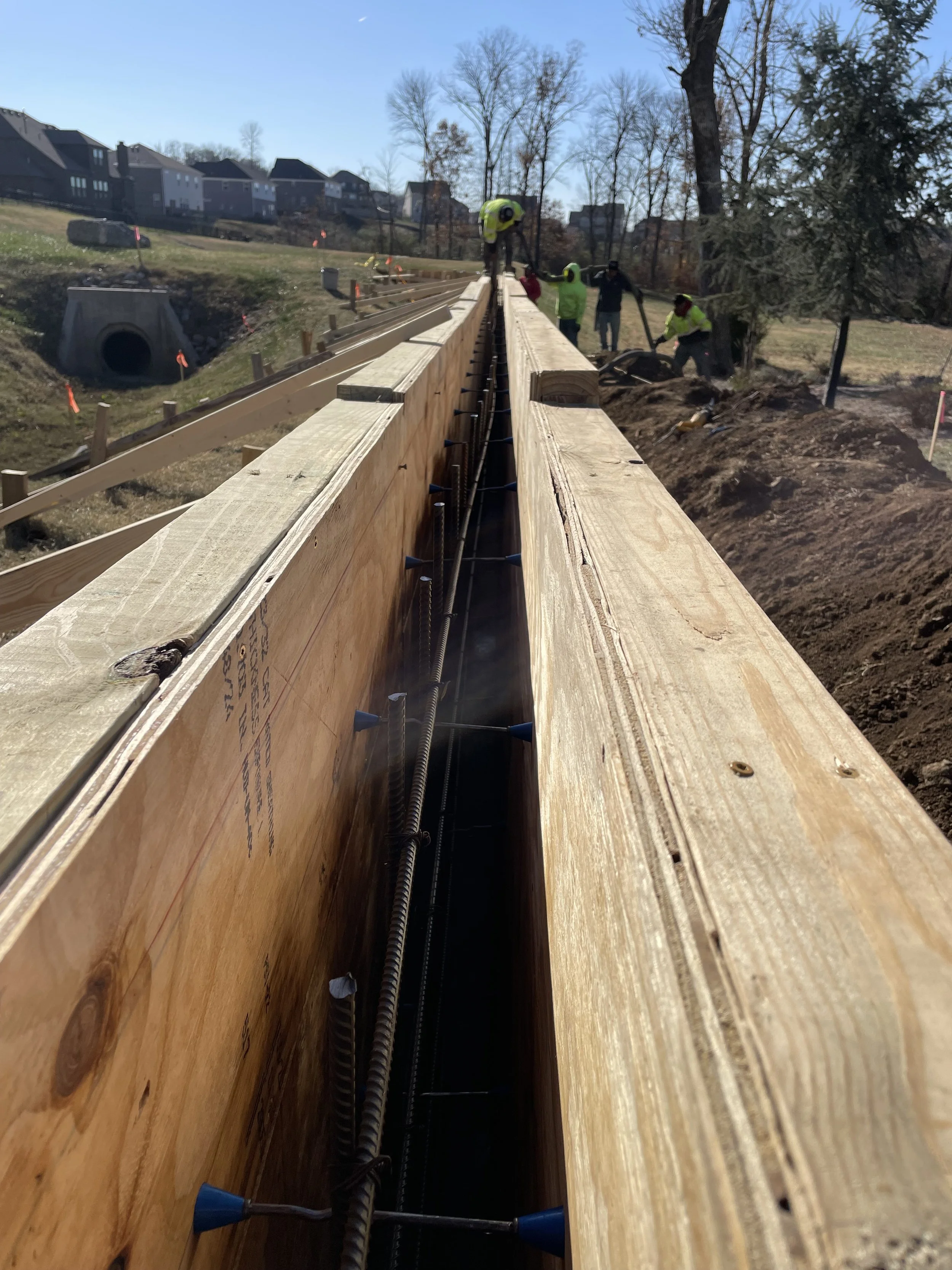 Workers at a construction site building a wooden structure, possibly a bridge, with metal rebar inside the wood.