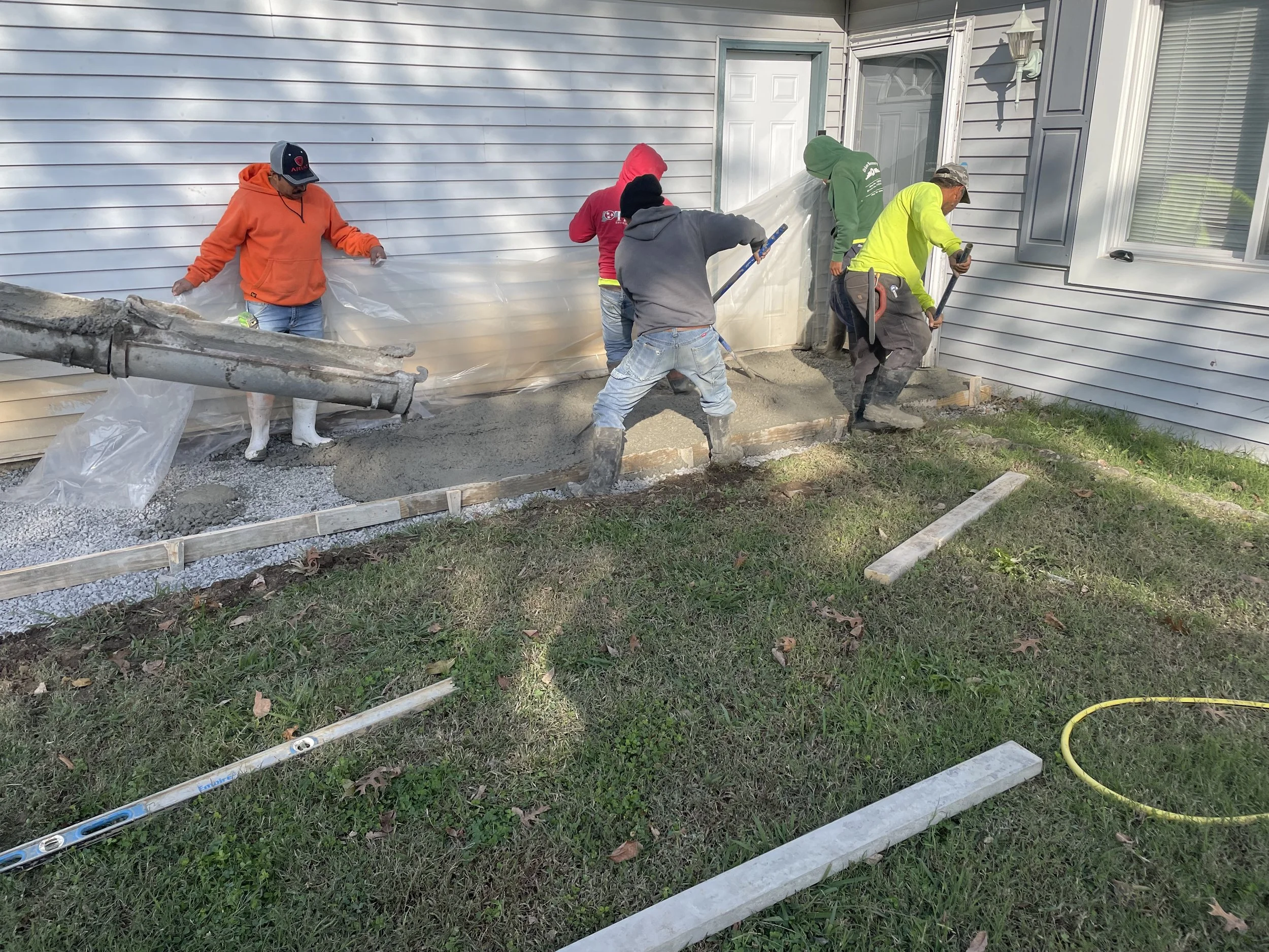 Construction workers pouring and spreading concrete to create a new walkway at the front of a house.