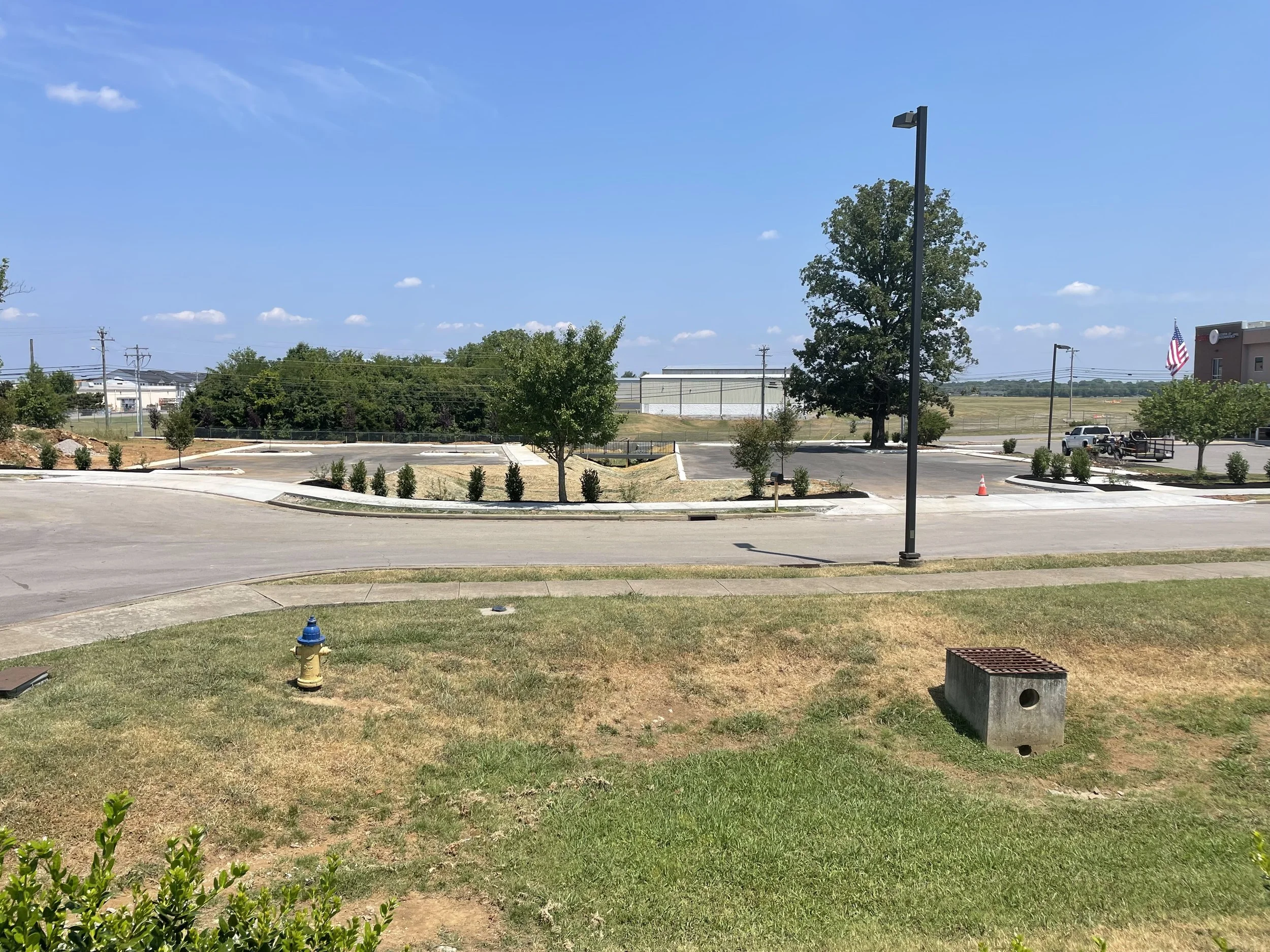 Empty parking lot with a street lamp, a fire hydrant, and some trees under a blue sky with a few clouds.