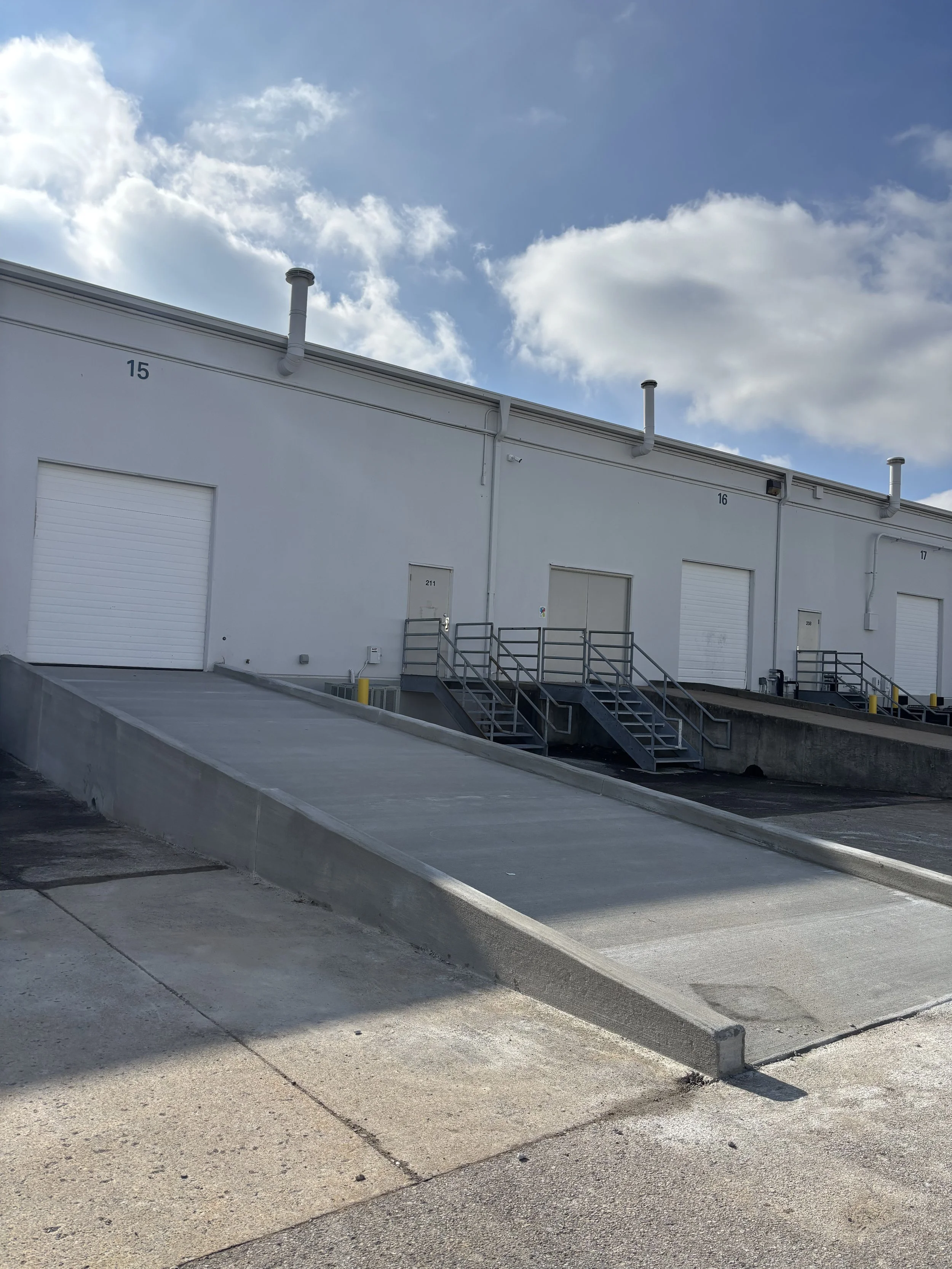 Loading dock with ramps and white warehouse doors under partly cloudy sky.