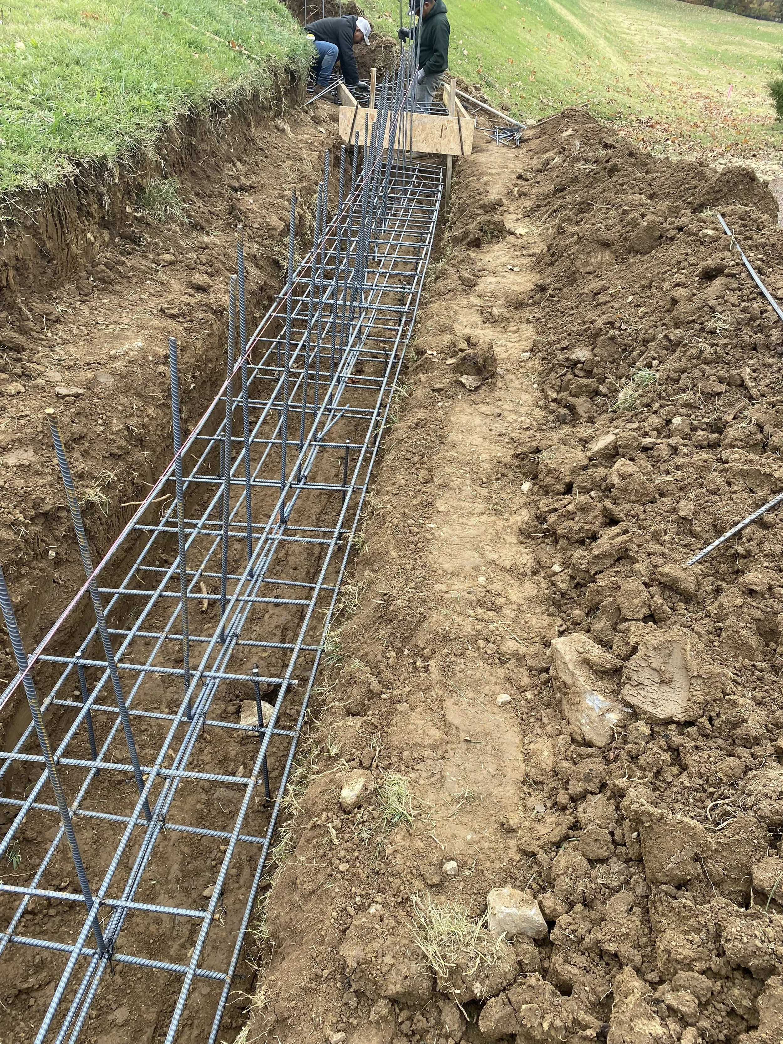 Construction workers installing steel reinforcement bars in a trench for a concrete foundation.