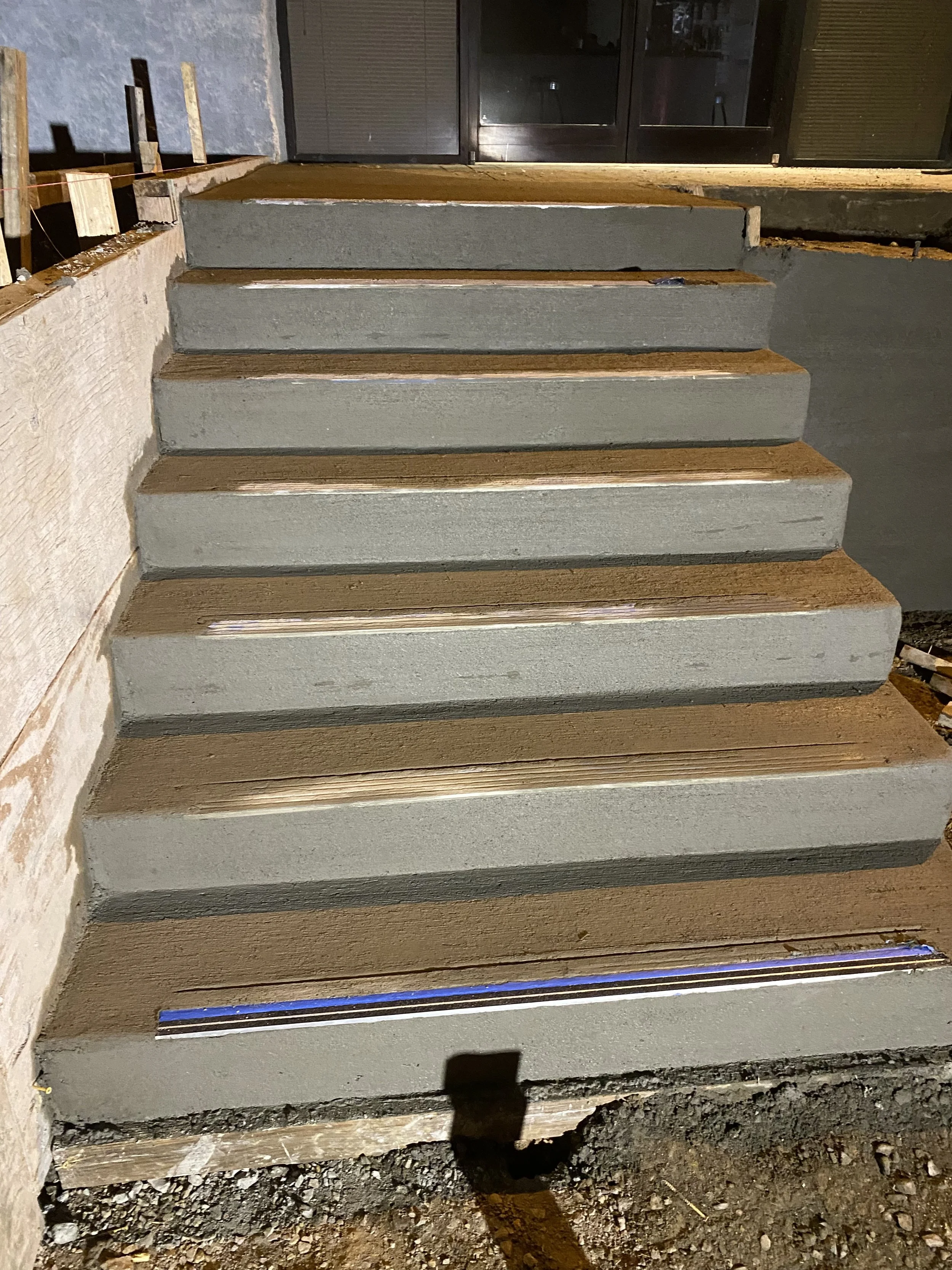 Concrete staircase under construction with wooden forms on sides, leading up to a glass door.