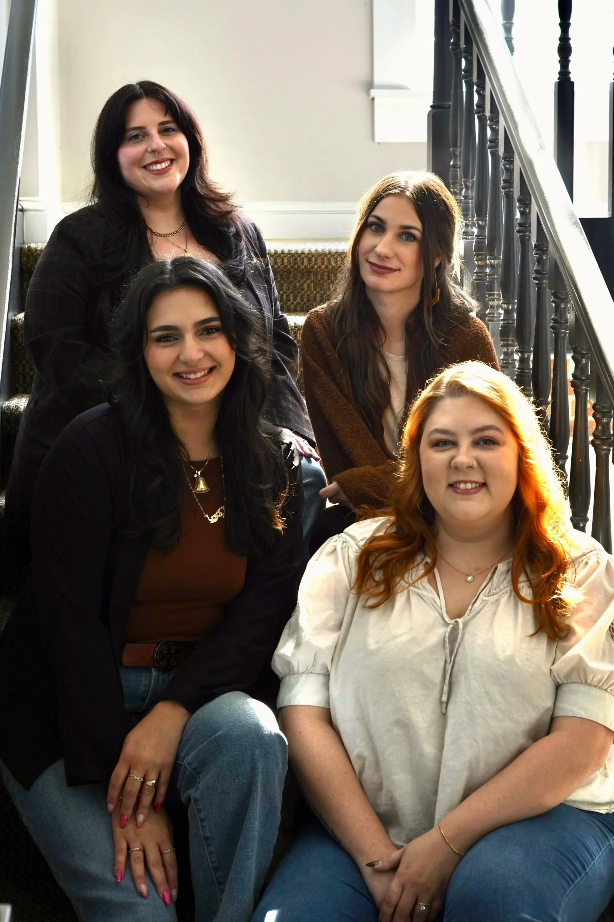 Group of five women sitting on stairs, smiling, in a well-lit indoor space.