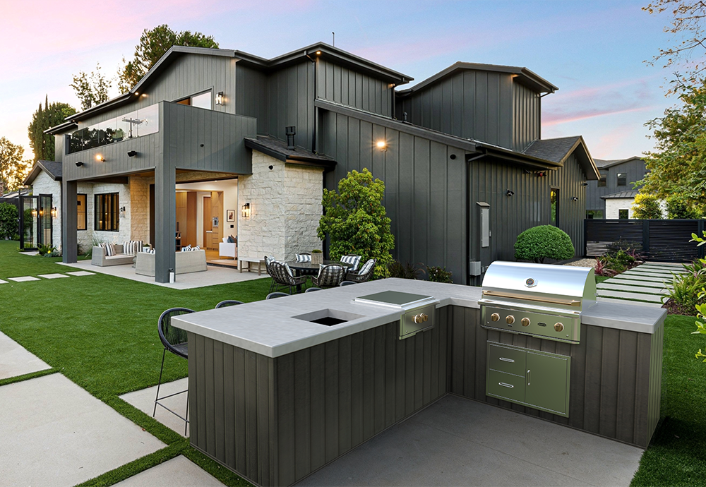 Modern backyard with outdoor kitchen, seating area, and green lawn at sunset
