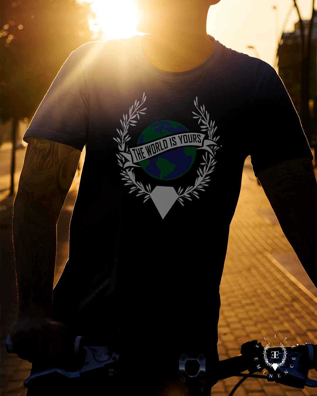 A person riding a bicycle during sunset, wearing a black t-shirt with a graphic of the Earth and the text 'The World is Yours'.