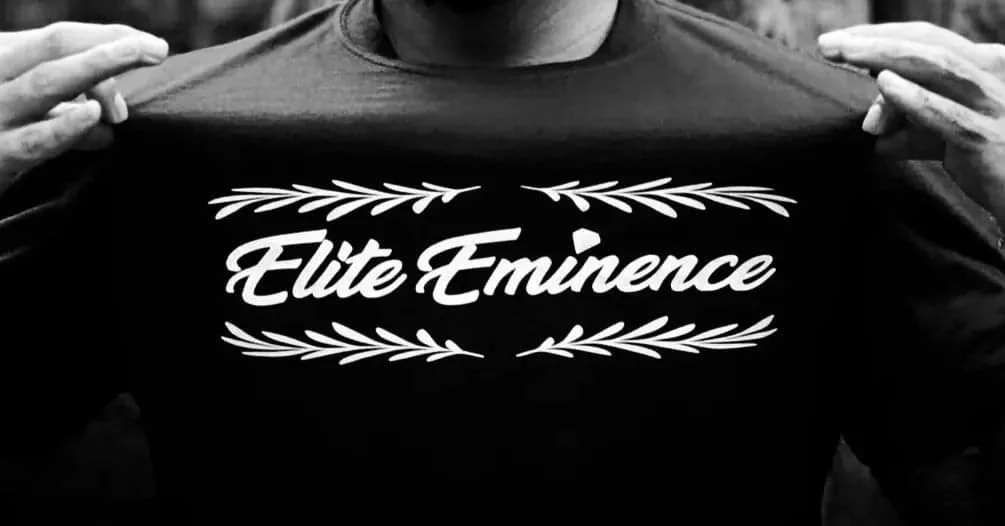 Person holding up a T-shirt with the words "Elite Eminence" and decorative leaves printed on it.