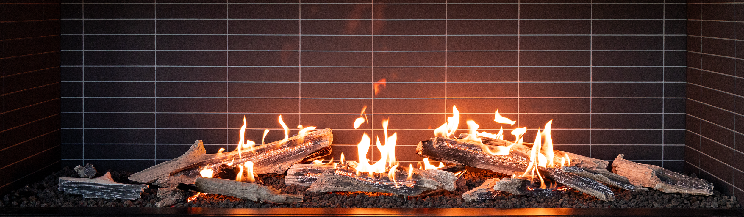 Modern fireplace with burning logs and flames, black tiled surround.