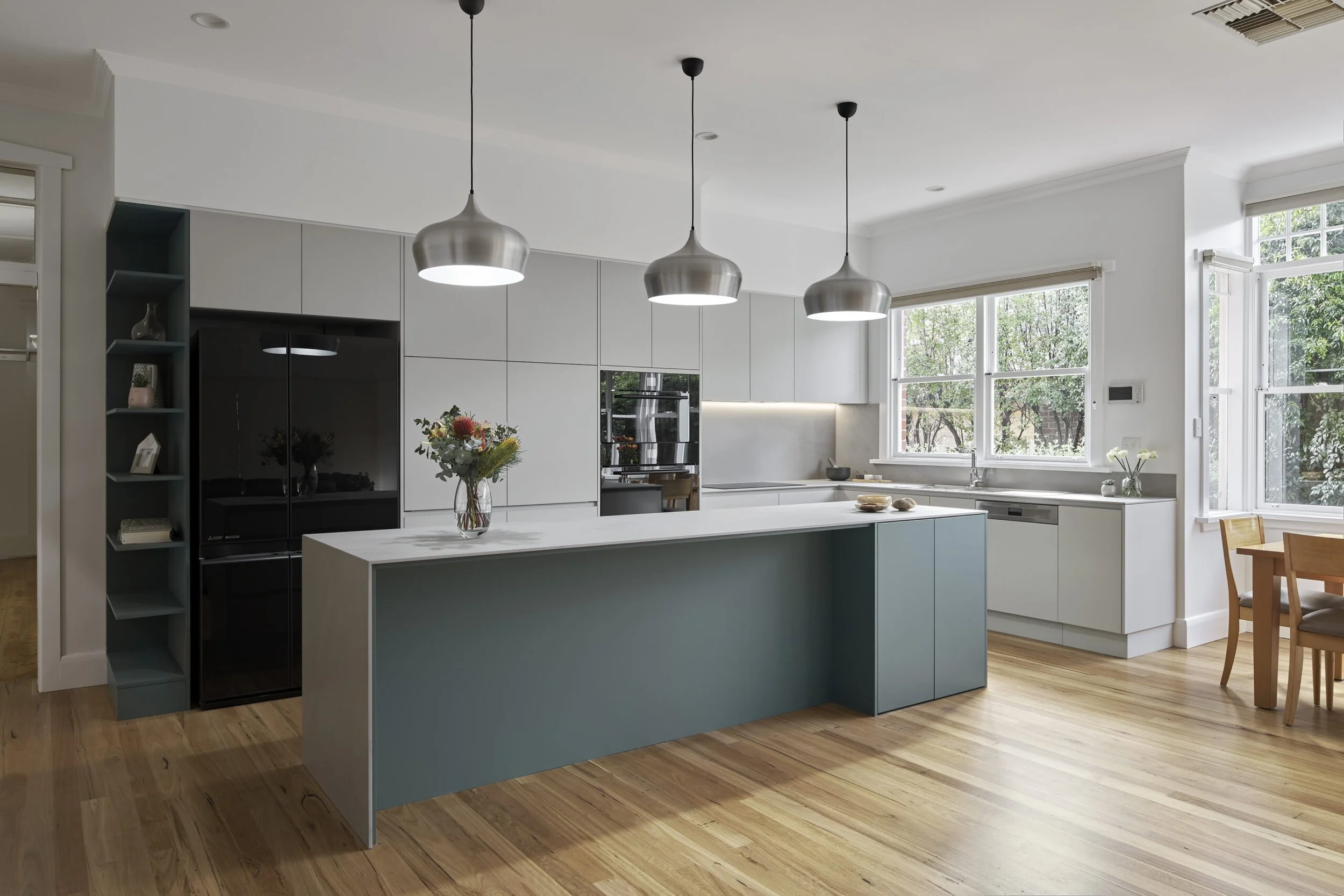 Modern kitchen with white cabinetry, a large island with a blue base, pendant lights, and hardwood floors.