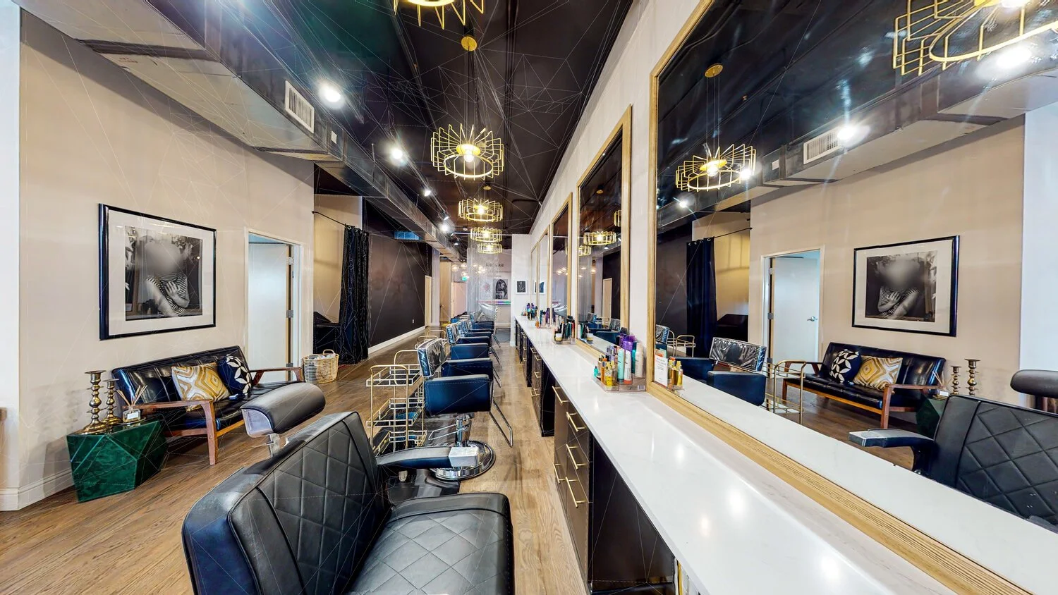 A modern salon with black and white decor, black chairs, a long mirror, and framed black-and-white photographs on the walls.