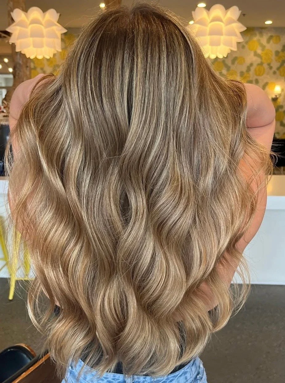 Woman with long, blonde, wavy hair inside a brightly decorated café or restaurant.
