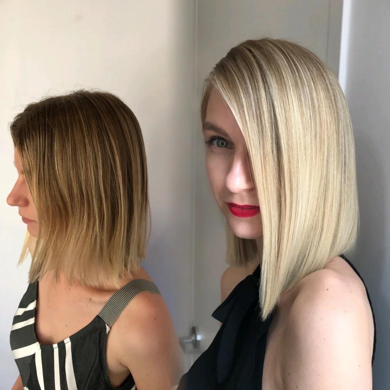 Two women with shoulder-length blonde hair, one with darker roots, standing back to back in front of a light-colored wall. The woman on the right has straight, shiny hair with a side part and is wearing red lipstick and a sleeveless black top.