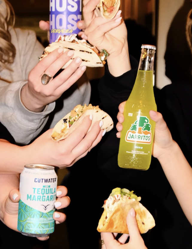 People holding tacos, a Jarritos lime soda, and a can of Cutwater tequila margarita.