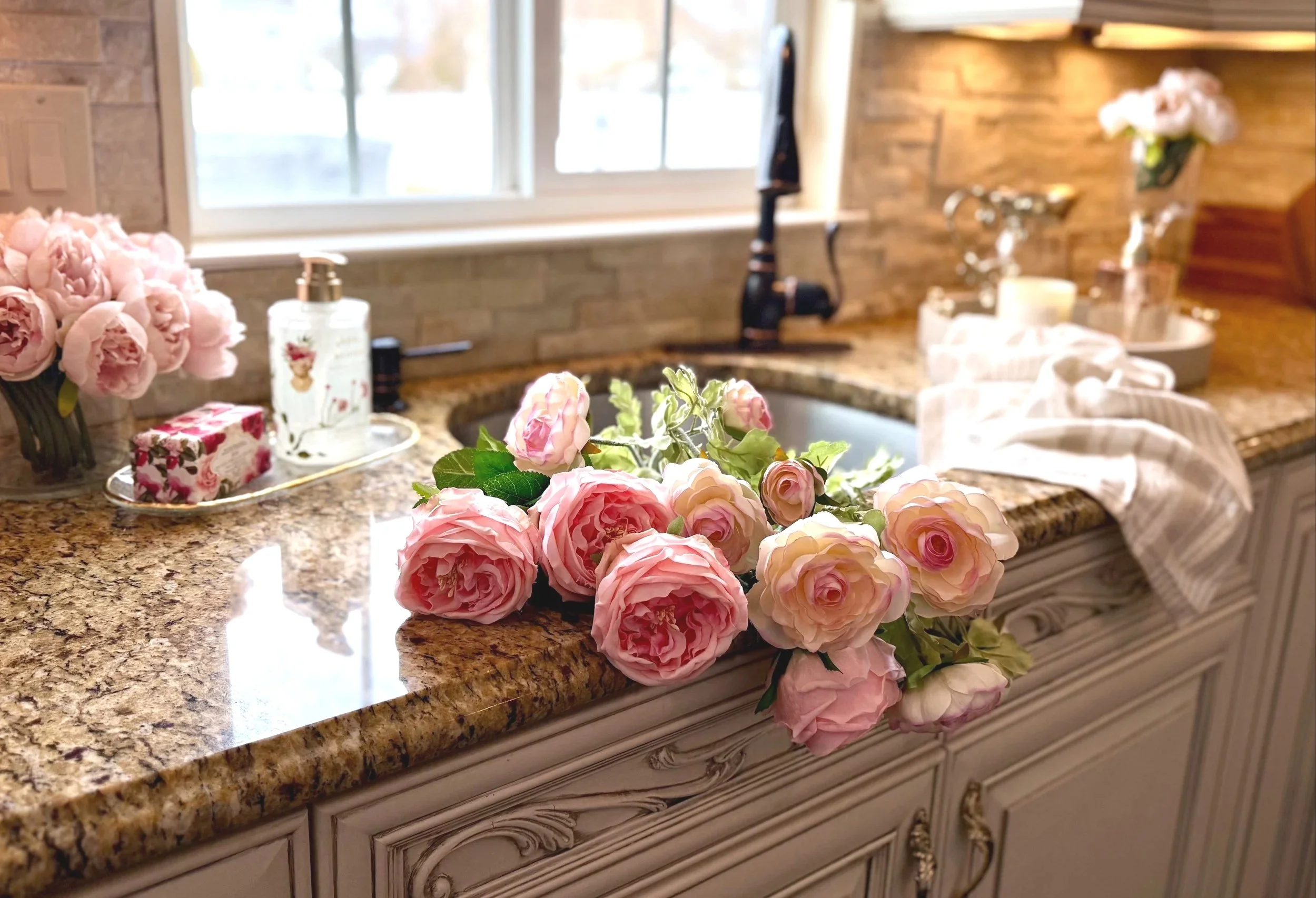 beautifully styled kitchen counter and sink with cascading pink flowers, decorative cabinets